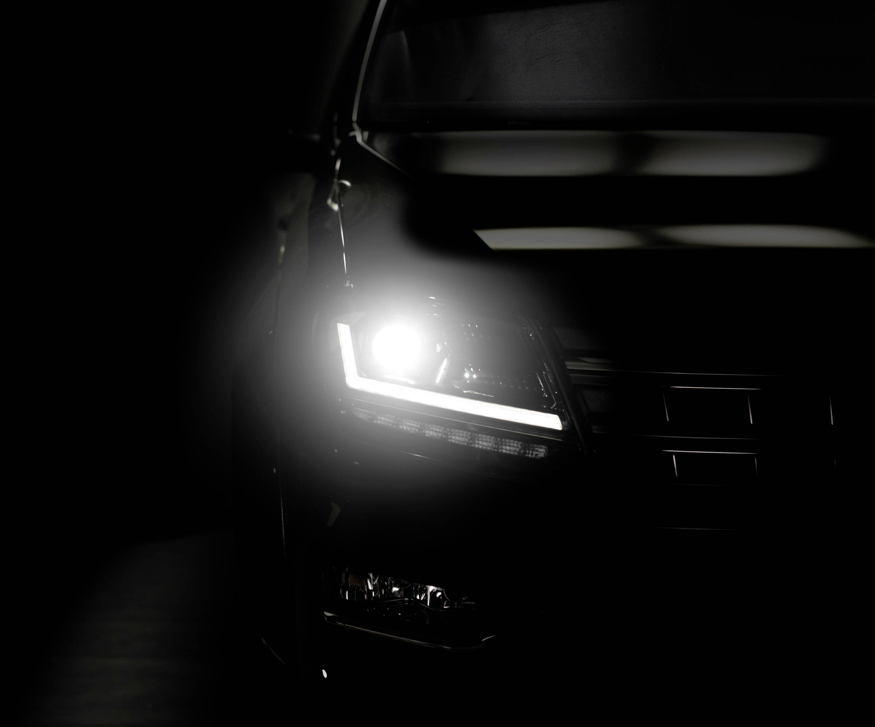 Halve vooraanzicht van een auto 's nachts, met een ingeschakelde koplamp die de voorgrond verlicht.