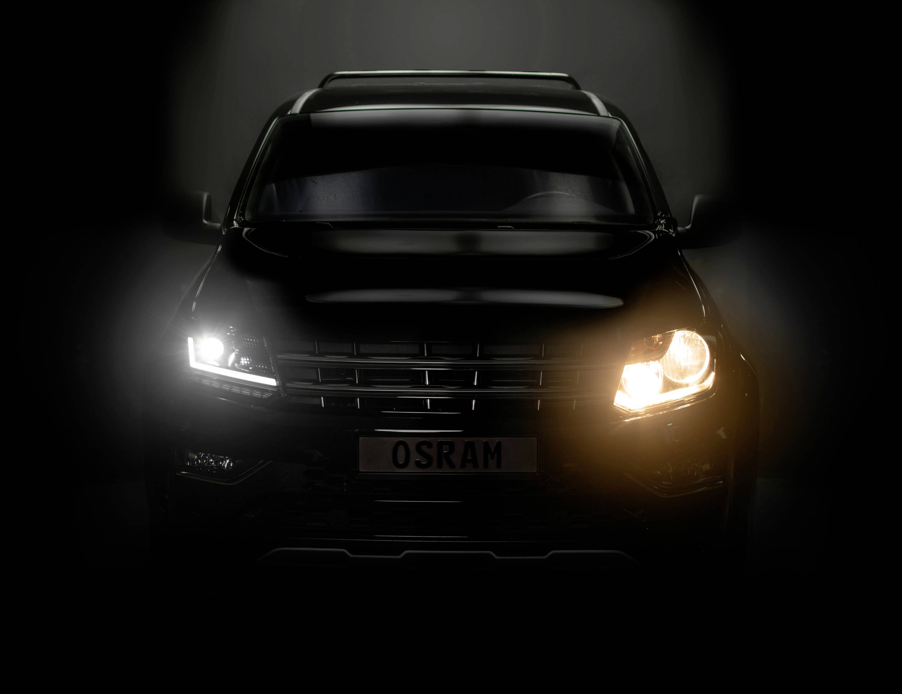 Een auto in het donker met een ingeschakelde OSRAM-koplamp rechts en een donkerder licht links, waarbij het frontdesign zichtbaar is.