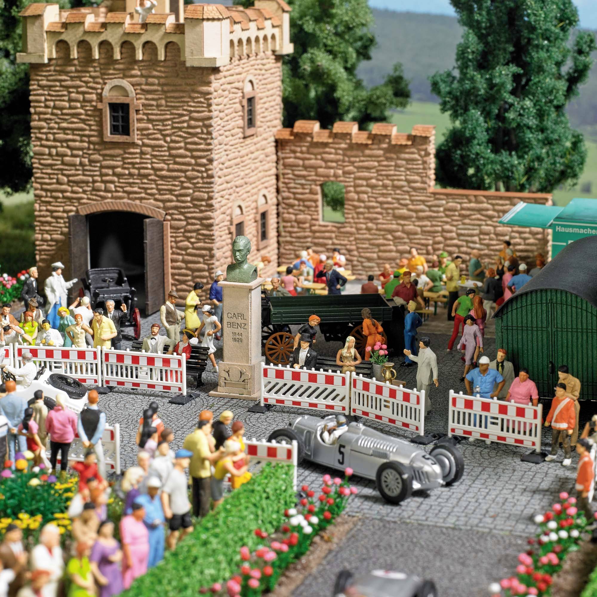 Een miniatuurmodel van een racescène toont een grijze raceauto, toeschouwers en historische gebouwen op de achtergrond.