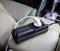 Stroomadapter met twee USB-poorten en één stopcontact, aangesloten in een auto. Ligt op een beige lederen stoel.