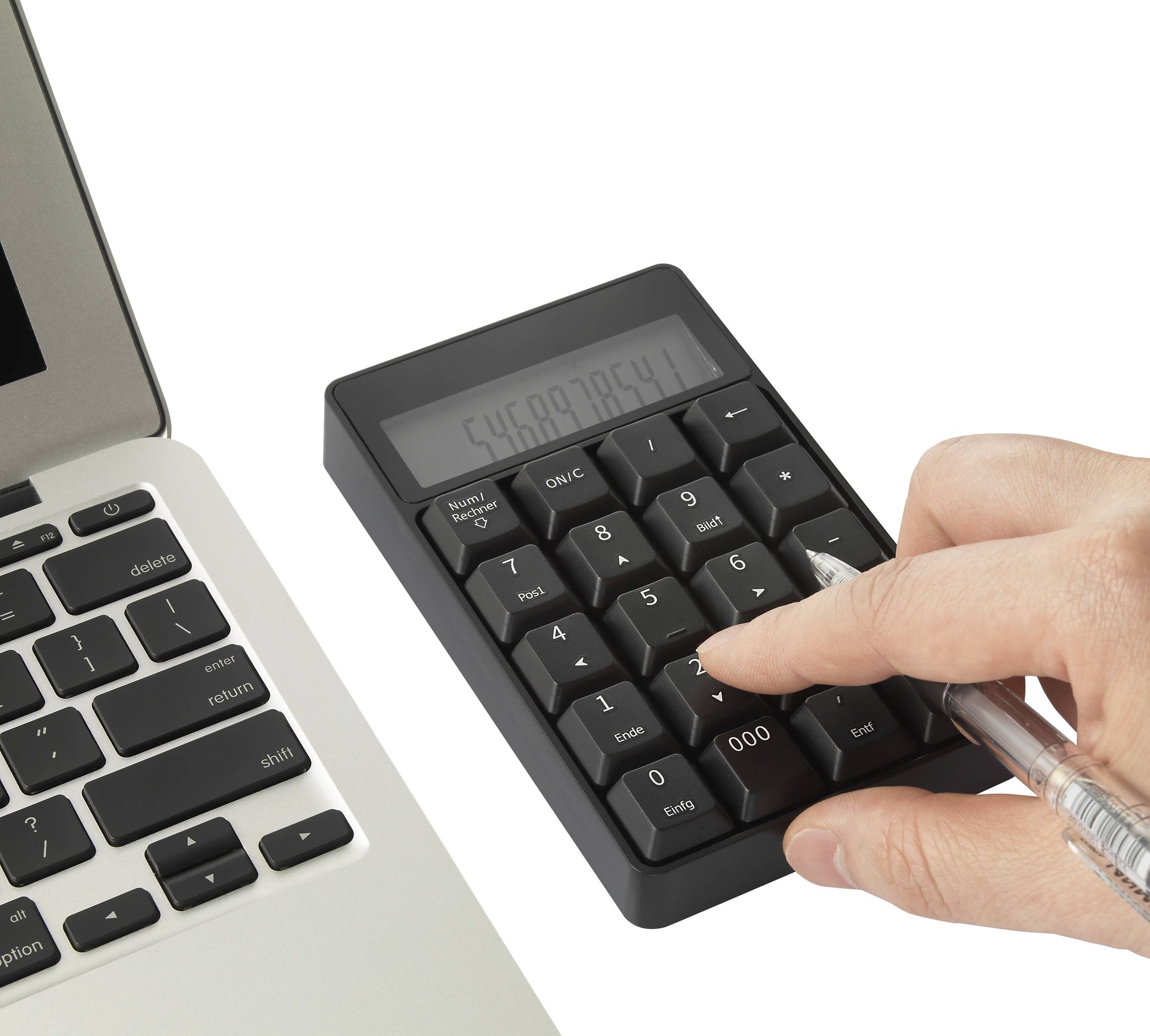 Een hand met een balpen tikt op een zwarte rekenmachine naast een laptop.