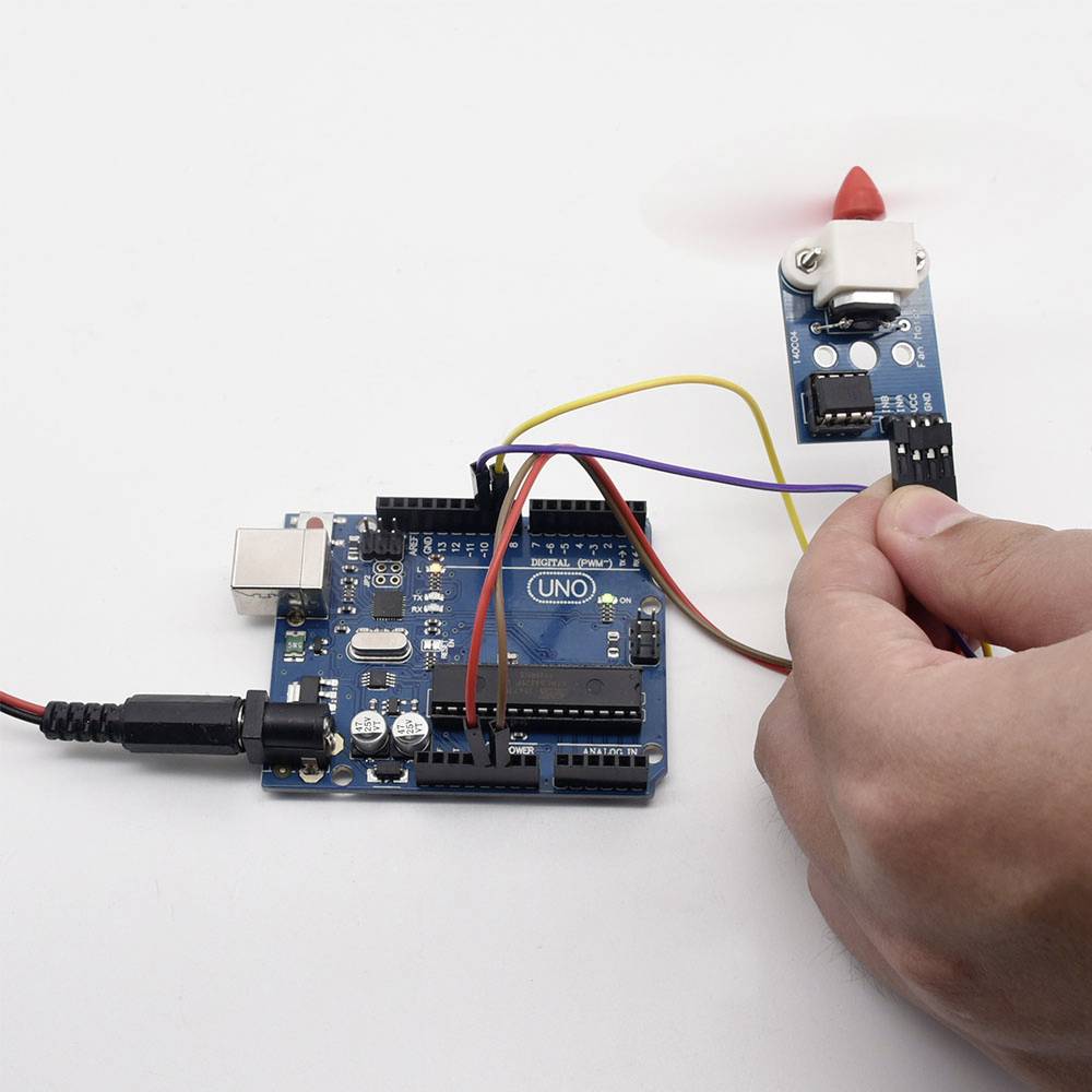 Een hand houdt een sensor vast die verbonden is met een Arduino-bord. Dunne kabels verbinden beide componenten voor een elektronica-project.