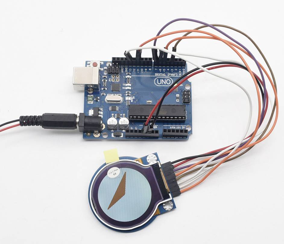 Microcontrollerprint met meerdere kabels en een aangesloten rond display dat een kompaspijl weergeeft.