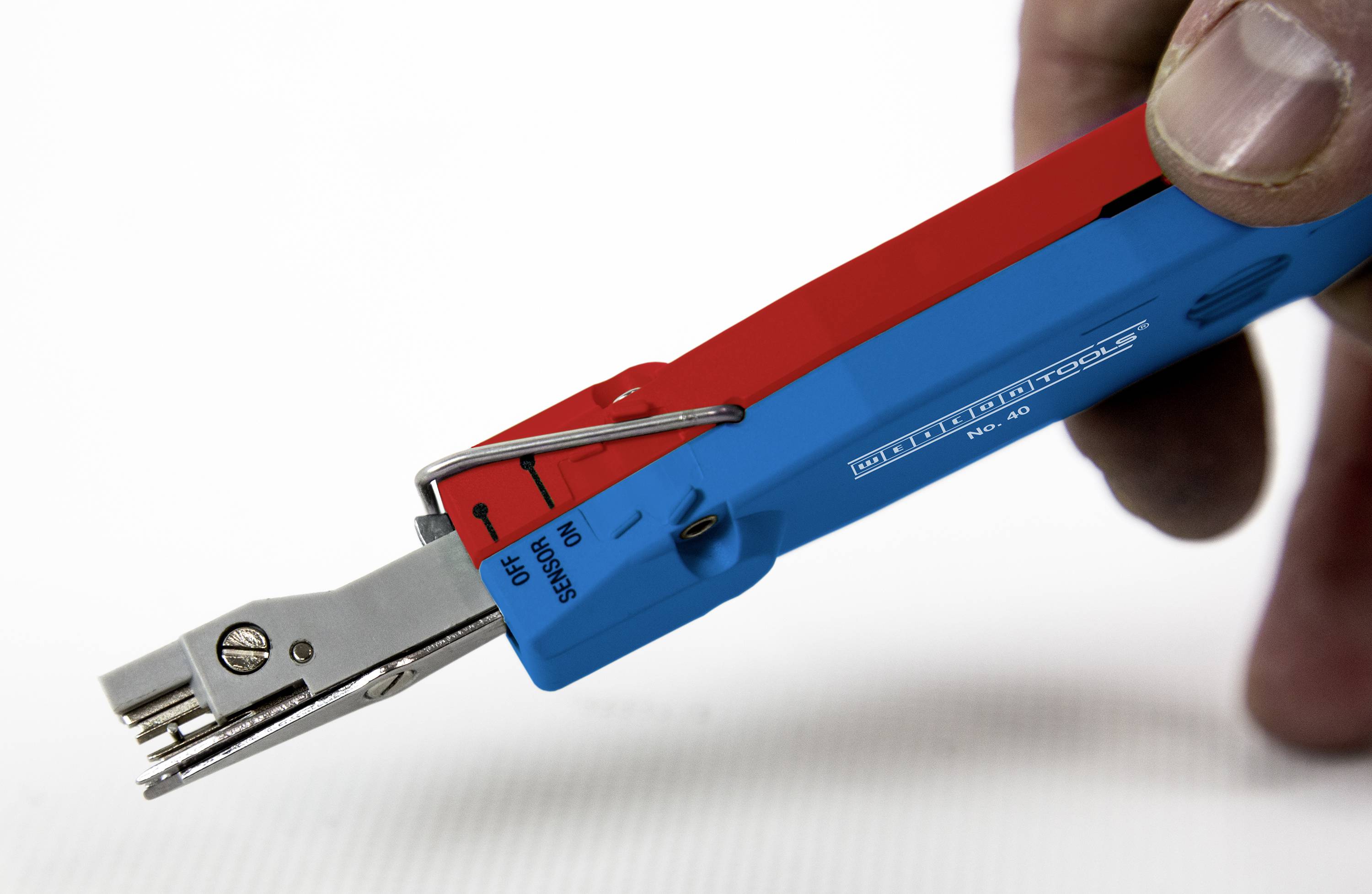 Een hand houdt een rood en blauw gereedschap voor het ontmantelen van kabels vast, met een mes en de inscriptie 'KELLY-probe'.