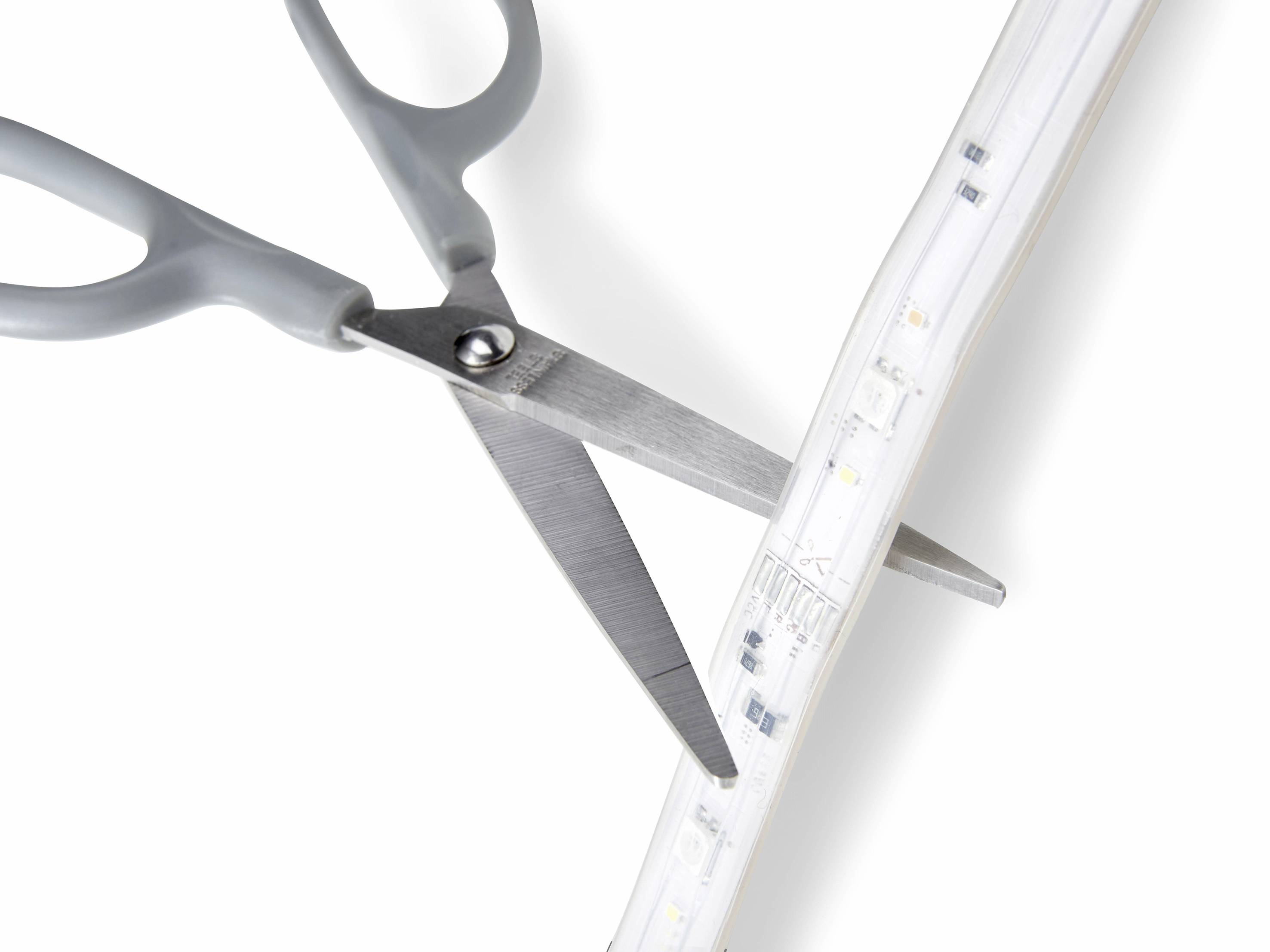 Een schaar snijdt door een verlicht LED-lint op een witte achtergrond.