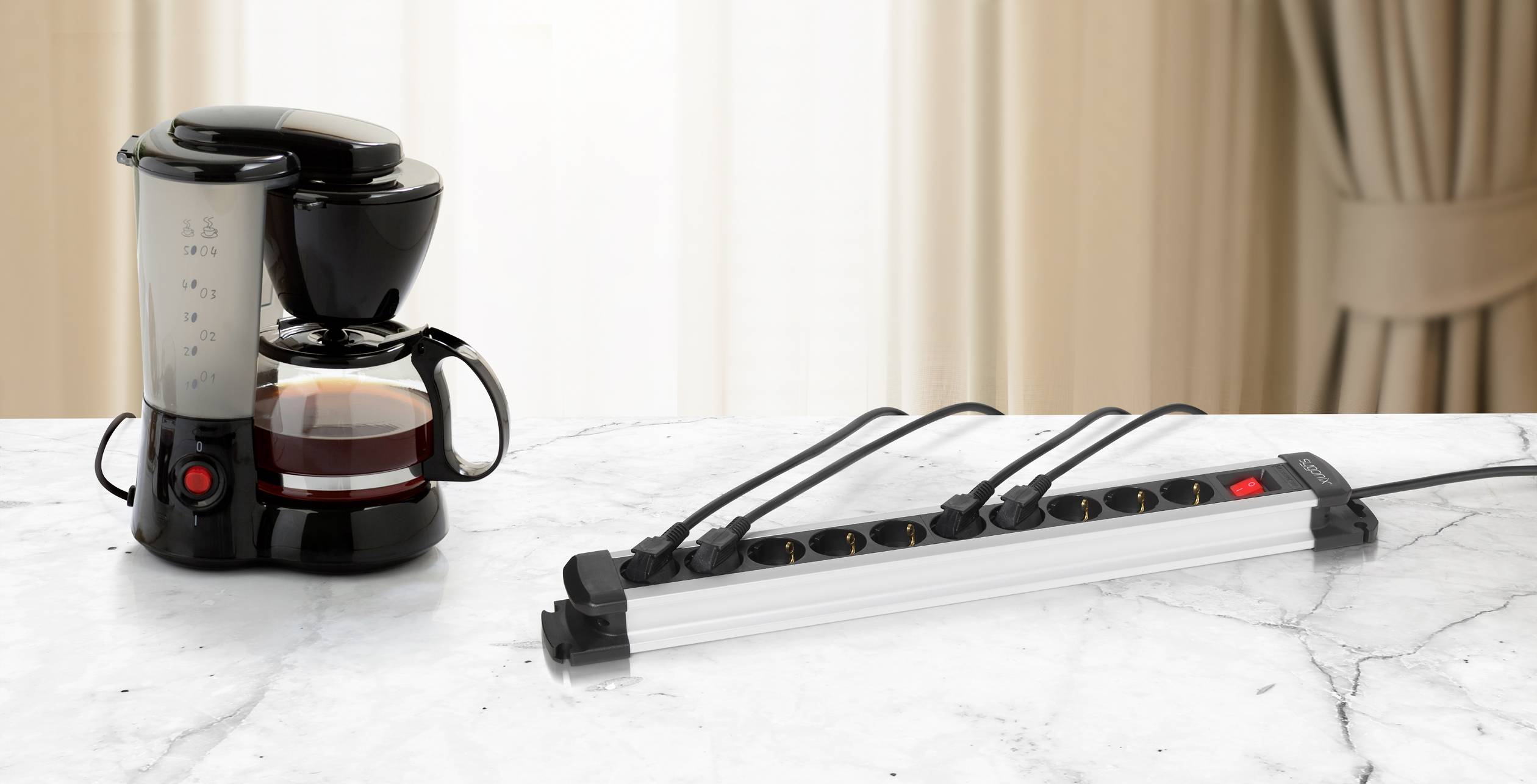 Koffiemachine op een marmeren tafel, naast een ingeschakelde stekkerdoos met meerdere aangesloten kabels.