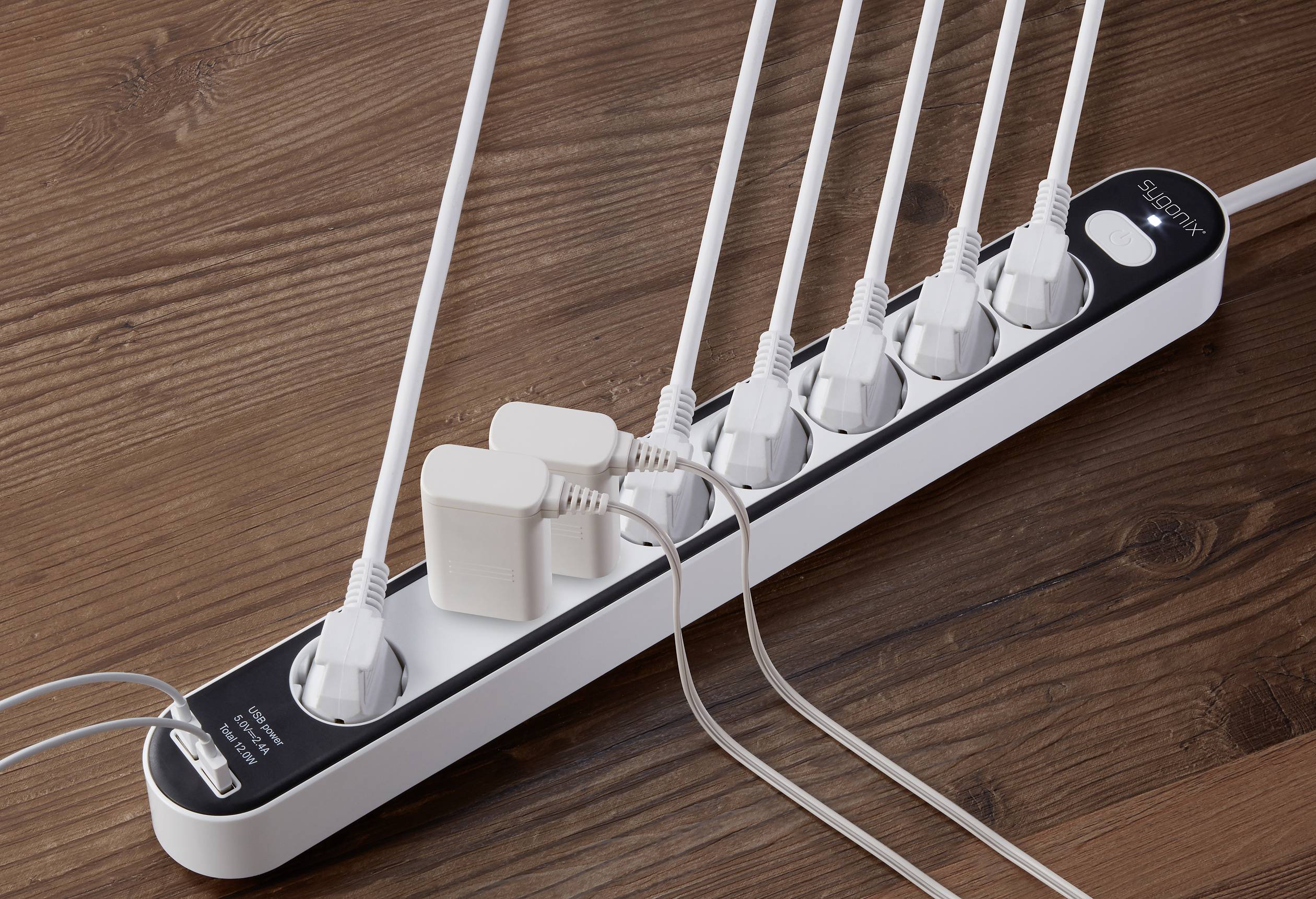 Stekkerdoos met negen aansluitingen, waarop meerdere witte kabels en adapters zijn aangesloten. Ligt op een houten tafel.