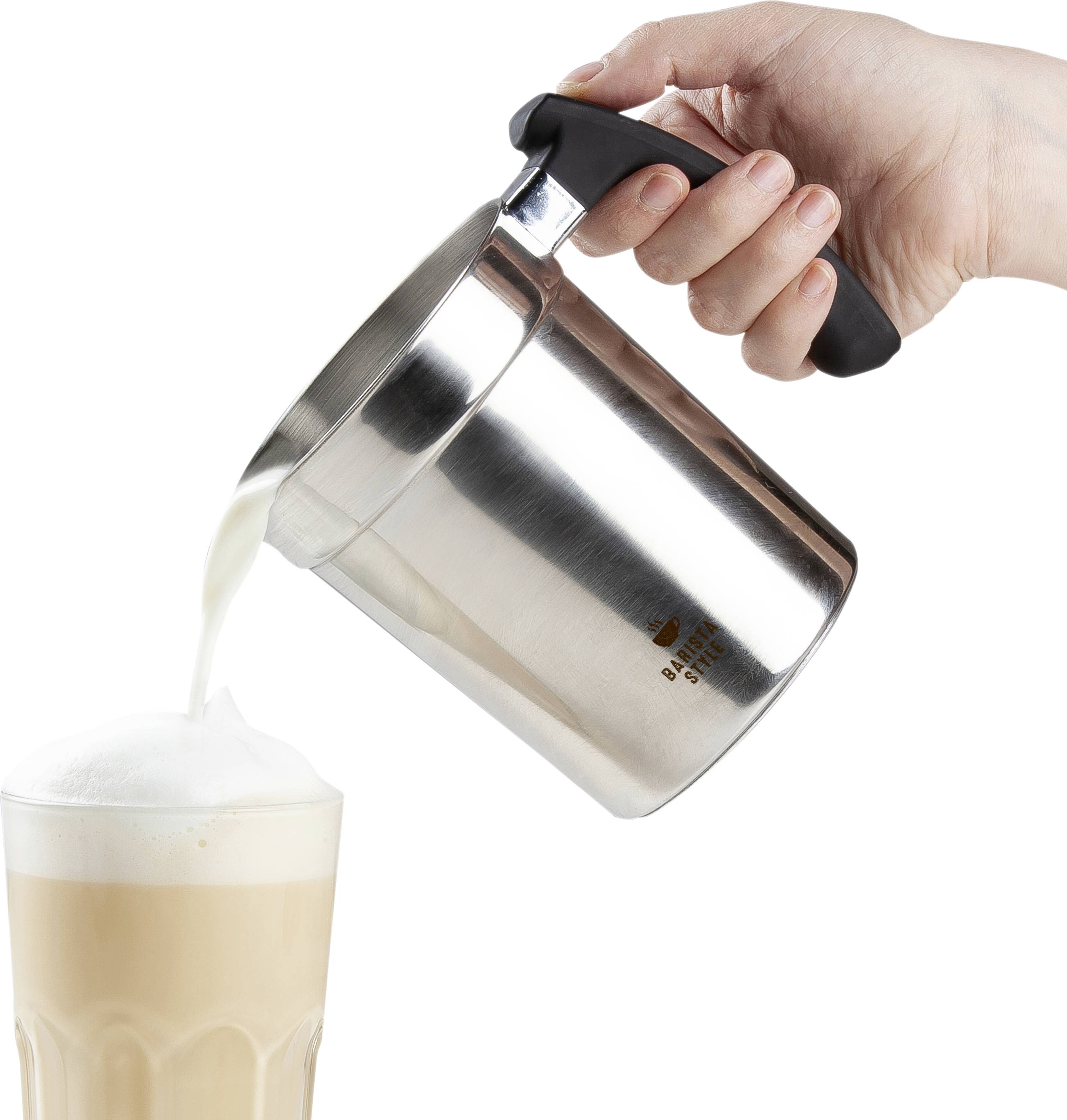 Een hand giet schuim uit een roestvrijstalen melkkannetje in een latte-glas dat op een tafel staat.