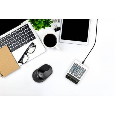 Laptop en tablet op een bureau, omringd door een notitieboek, bril, koffiekopje, muis en een oplader met batterijen.