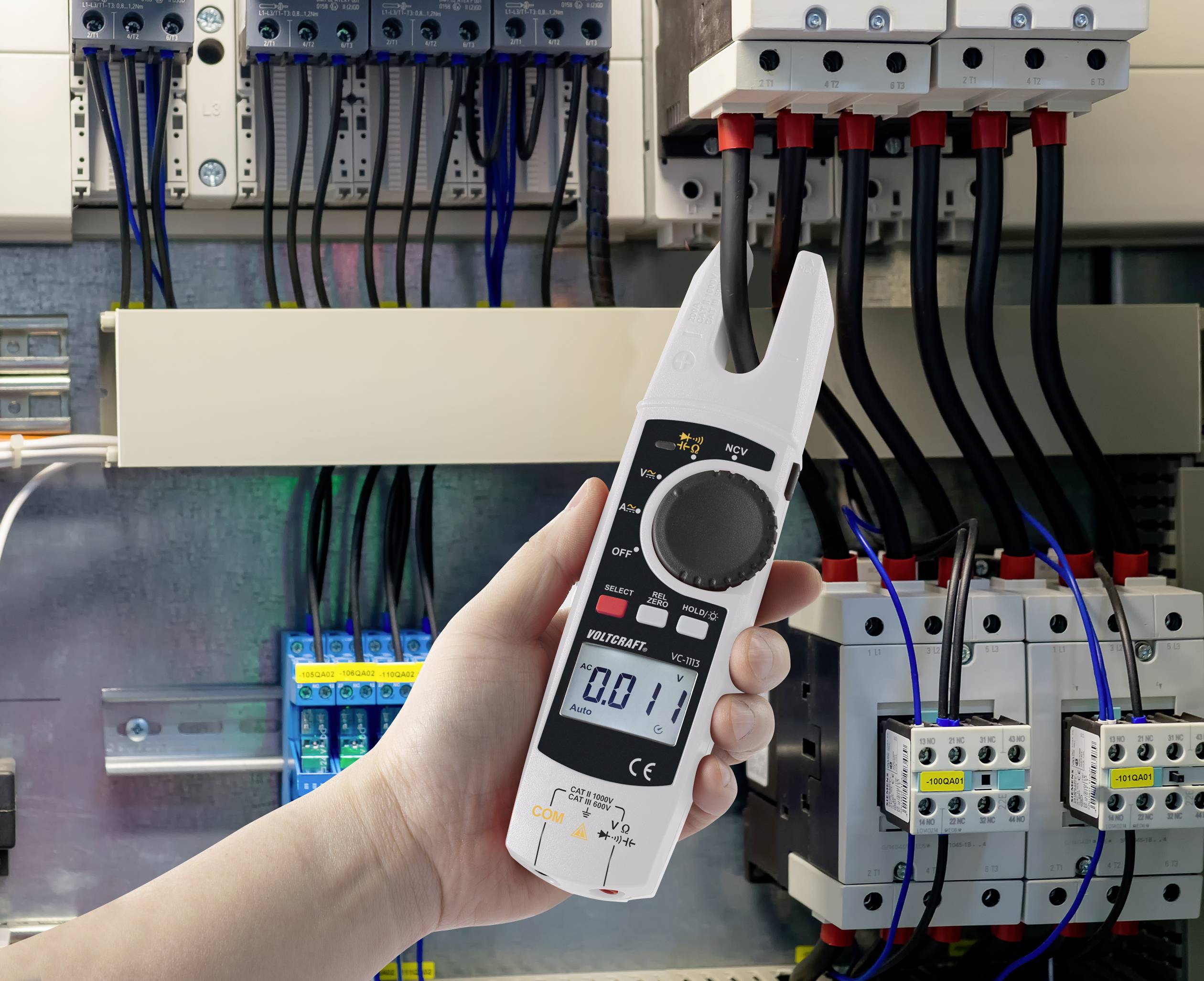 Een hand houdt een digitale multimeter vast die wordt gebruikt in een elektrische schakelkast om spanning of stroomsterkte te meten.