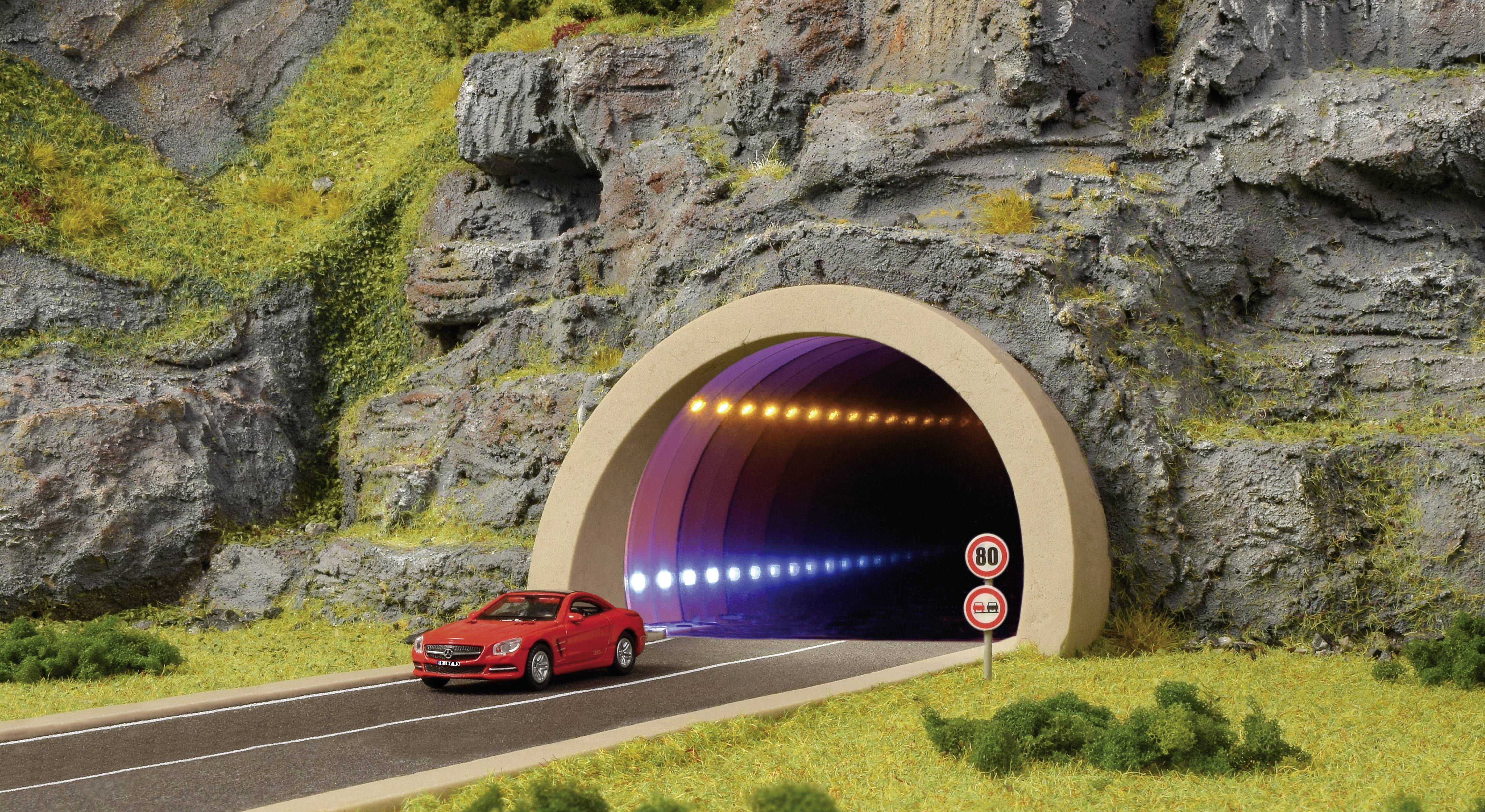 Een rode auto rijdt uit een verlichte tunnel in een bergachtig landschap. Het verkeersbord geeft een snelheidslimiet aan van 80 km/u.