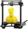 Een 3D-printer drukt een grote, gele standbeeld van een boomachtig wezen met armen en een gezichtsuitdrukking.