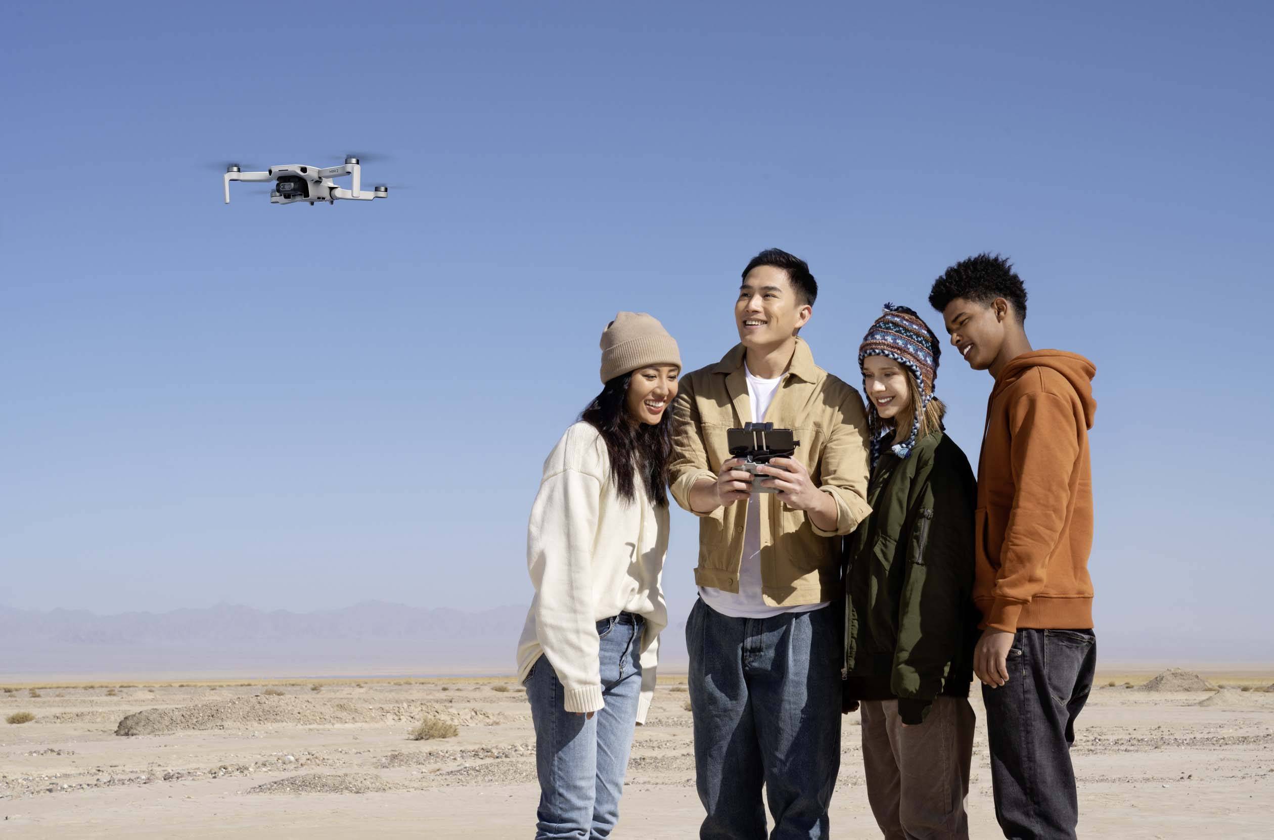 Vier personen staan in de woestijn en kijken naar een smartphone. Een drone vliegt op de achtergrond aan de blauwe lucht.