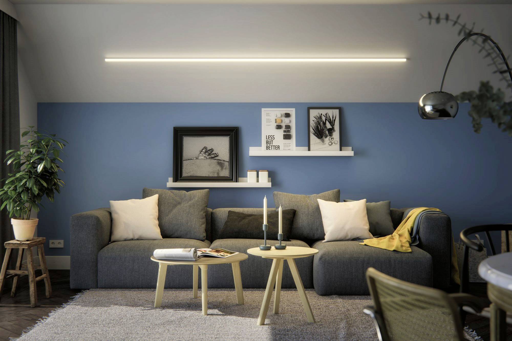 Een woonkamer met een grijze bank, blauwe accentmuren en minimalistische decoratie. Twee kleine ronde tafels staan voor de bank.