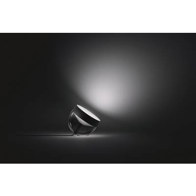 Een ronde, transparante lamp ligt op een donker oppervlak. Een zacht licht straalt schuin opzij en verlicht de achtergrond.