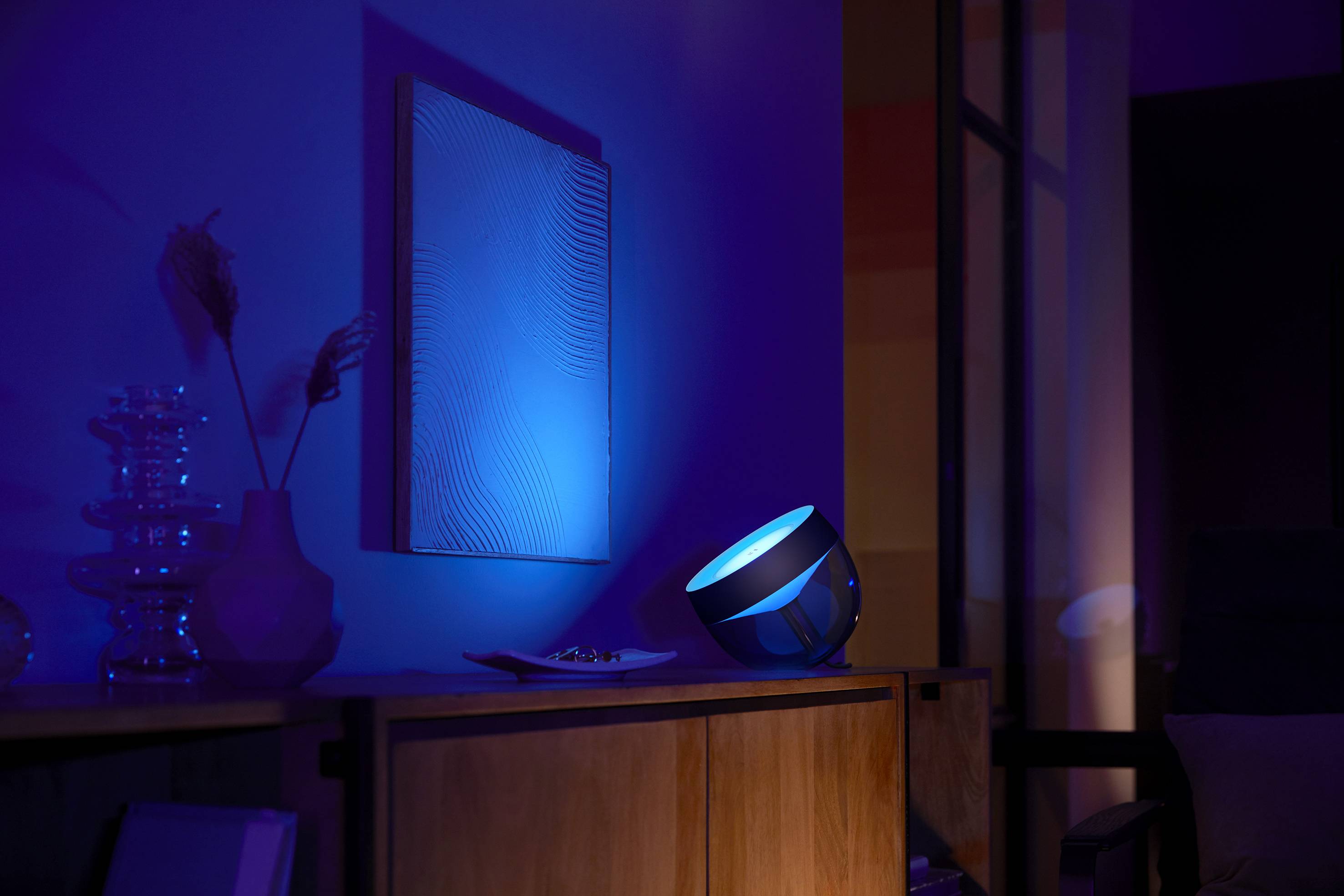Een slimme projector werpt blauw licht op een witte muur en verlicht daarmee een modern woonvertrek met meubels en decoraties.