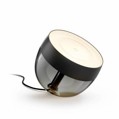 Een moderne tafellamp met een rond, zwart voetstuk en een transparante kap, liggend gepositioneerd. Een ingeschakeld LED-licht straalt warm naar boven.