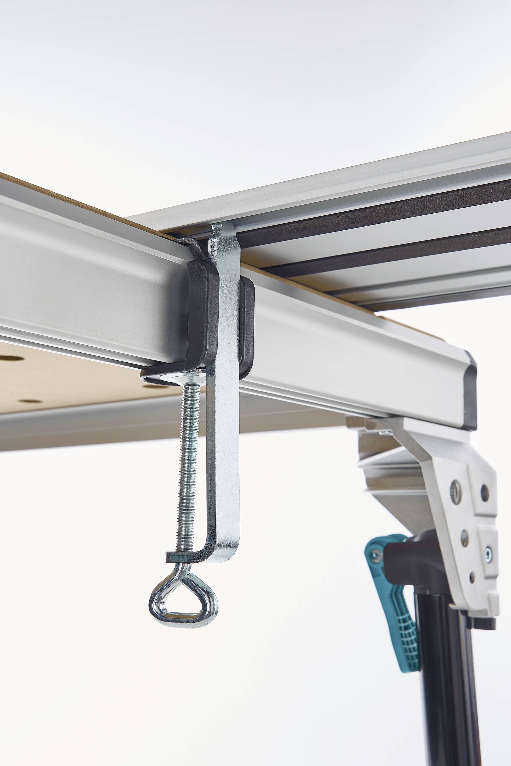 Metalen klem bevestigt een tafelblad aan een aluminium frame. De klem is stevig aangedraaid en stabiliseert de constructie.