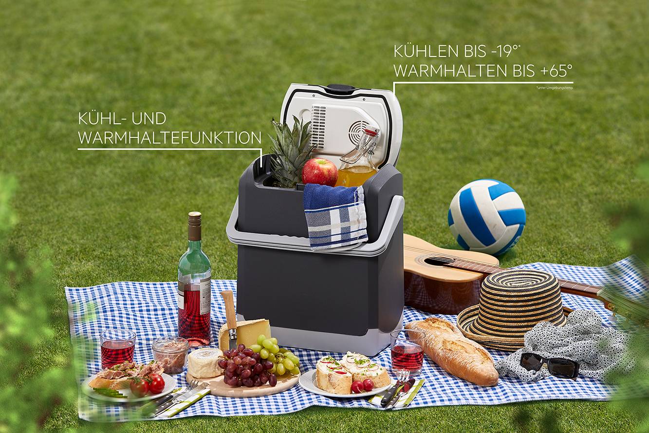 Een koelbox staat op een picknicklaken met eten zoals wijn, kaas, druiven en brood. Op de achtergrond een volleybal en een gitaar.