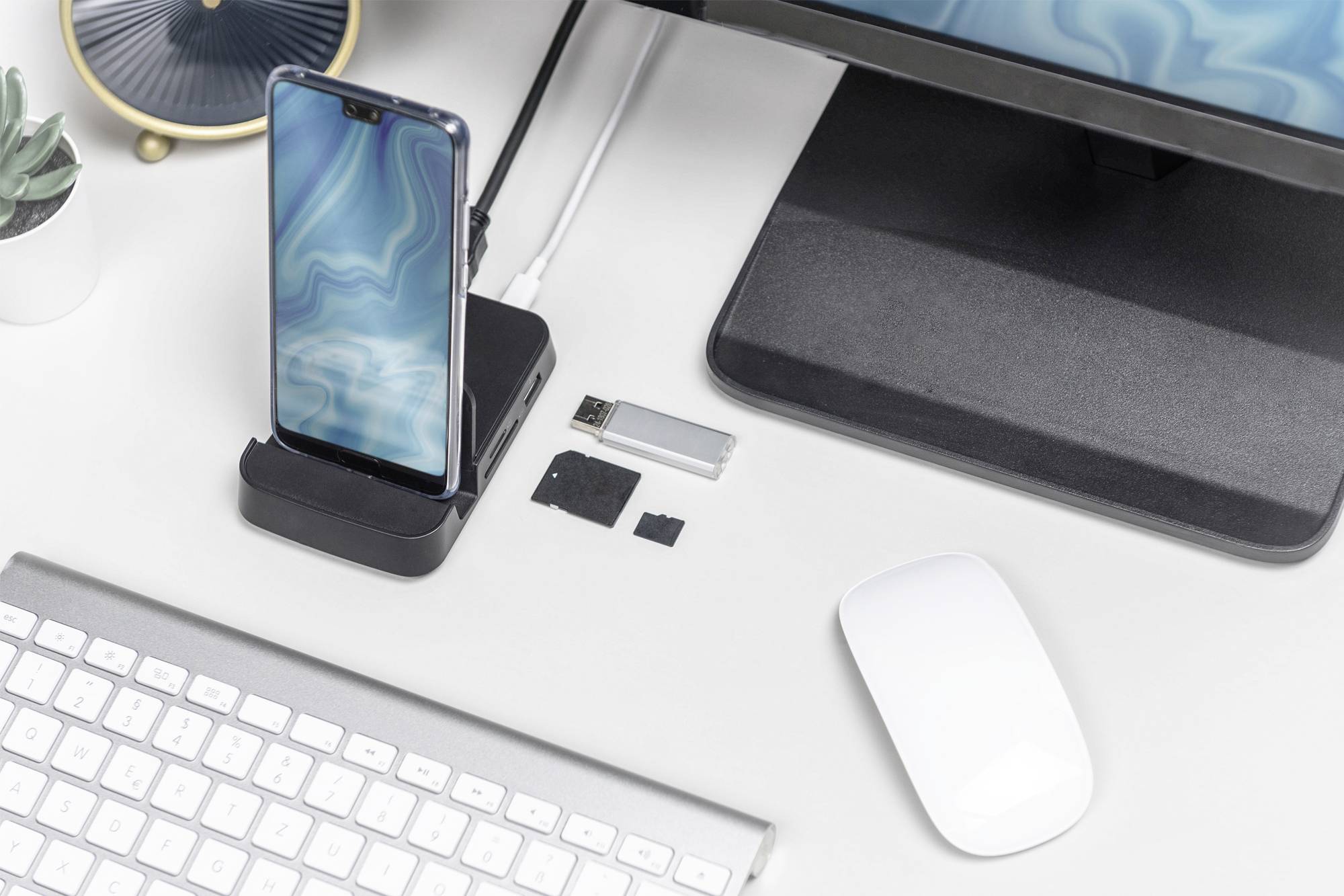 Een bureau met een smartphone op een dockingstation, USB-stick, geheugenkaart, toetsenbord en muis. Een monitor is zichtbaar.