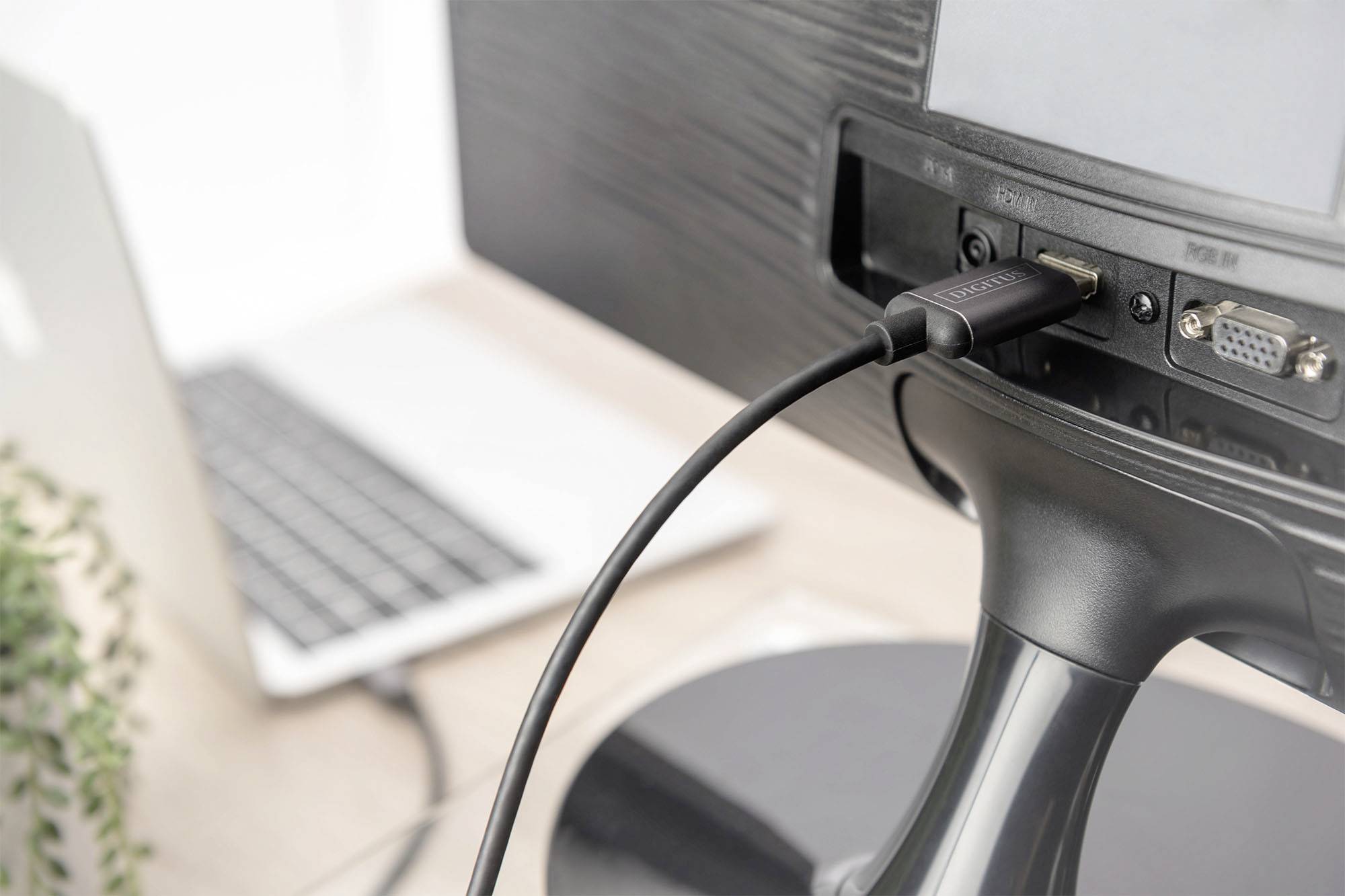 Een computerscherm is via een HDMI-kabel verbonden met een laptop. Op de voorgrond is een deel van het bureau zichtbaar.