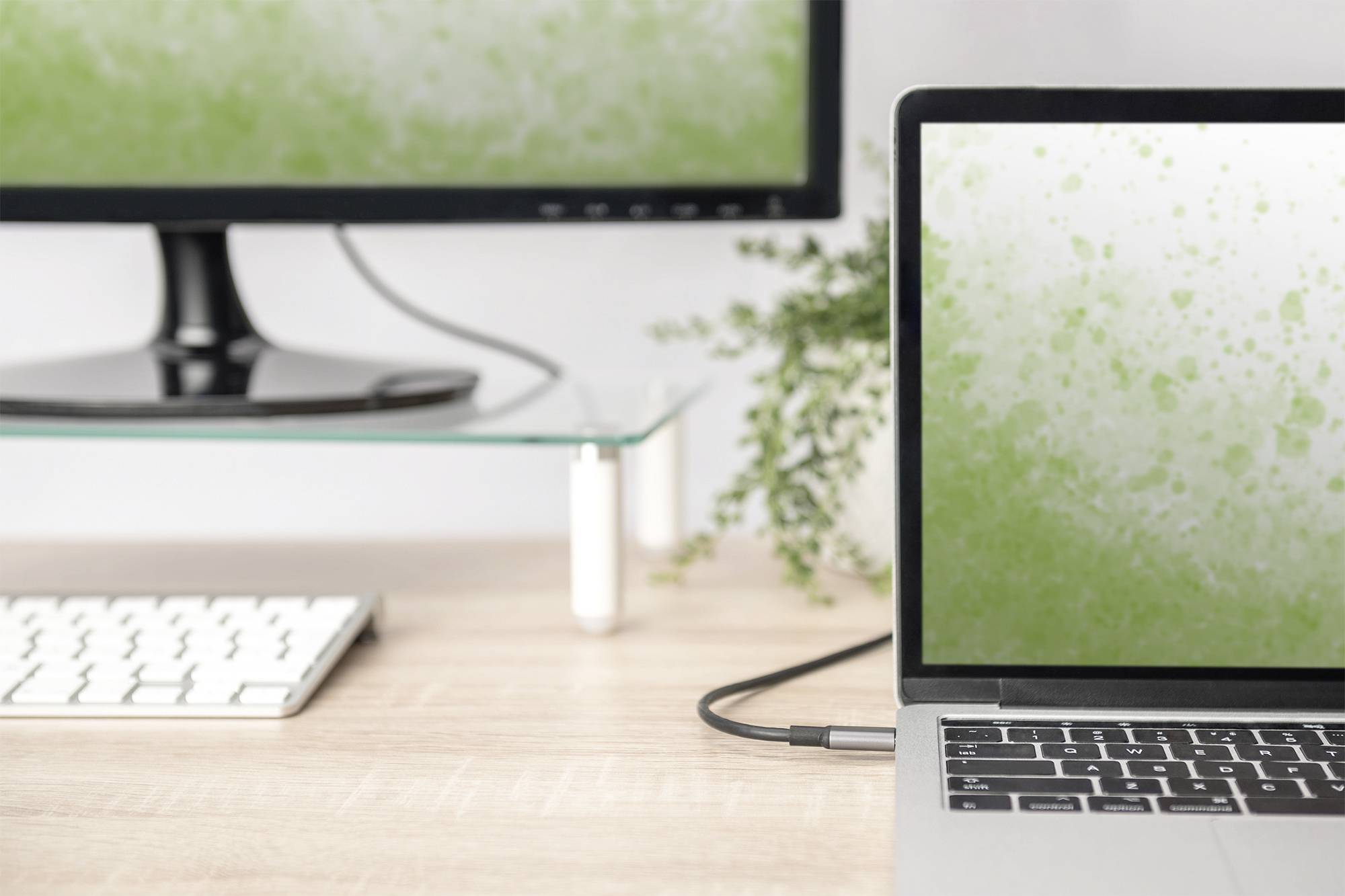Een laptop en een monitor op een bureau, waarbij beide schermen een groen spatpatroon tonen. Op de achtergrond een plant.