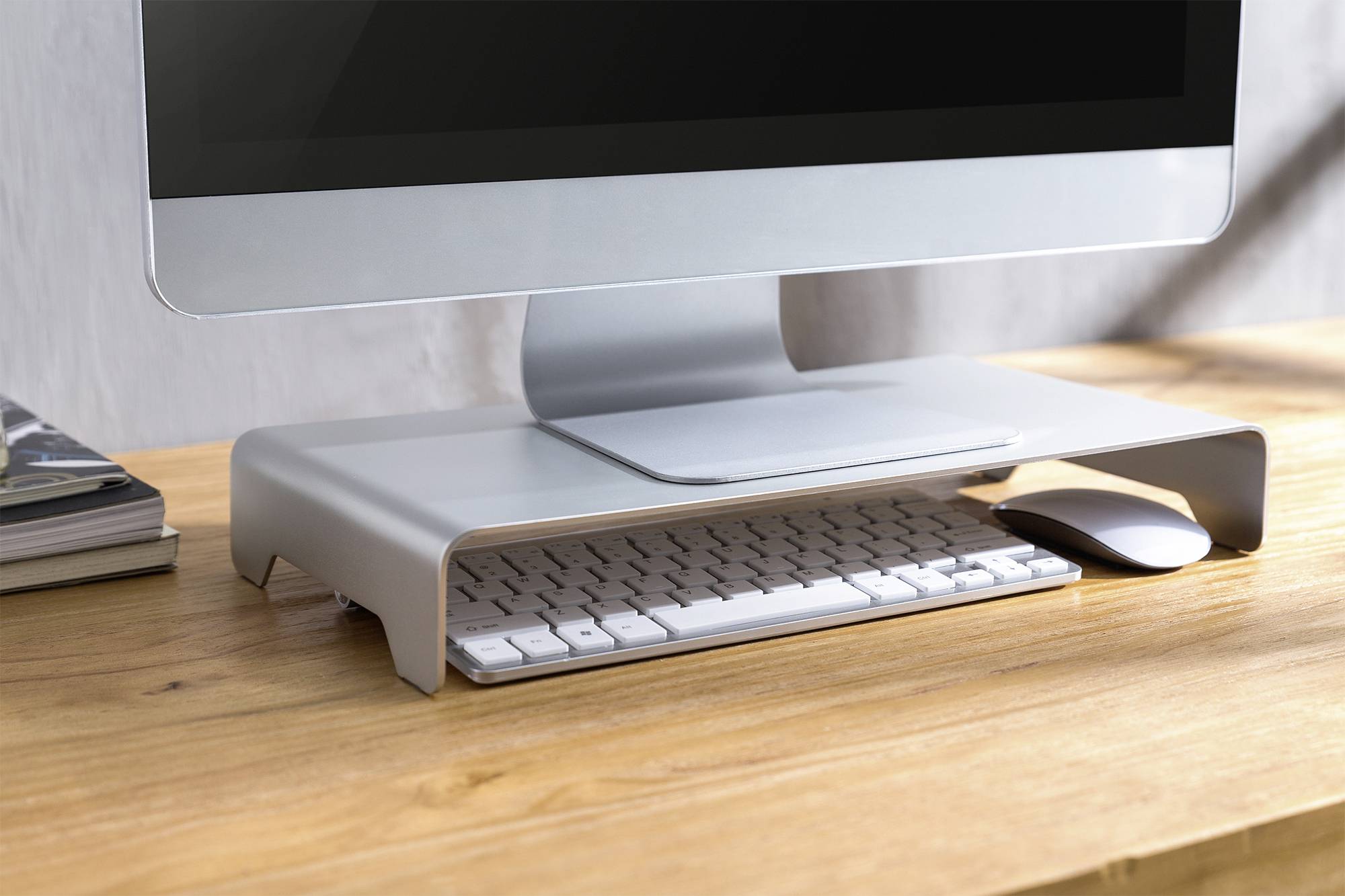 Een computermonitor staat op een grijze standaard op een houten tafel. Daaronder zijn een toetsenbord en een muis geplaatst.