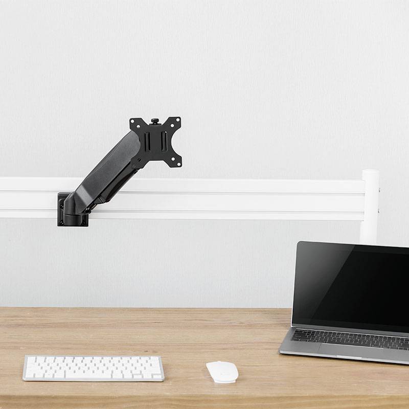 Een lege monitorarm staat op een bureau met een toetsenbord, een muis en een opengeslagen laptop, allemaal in een minimalistische omgeving.