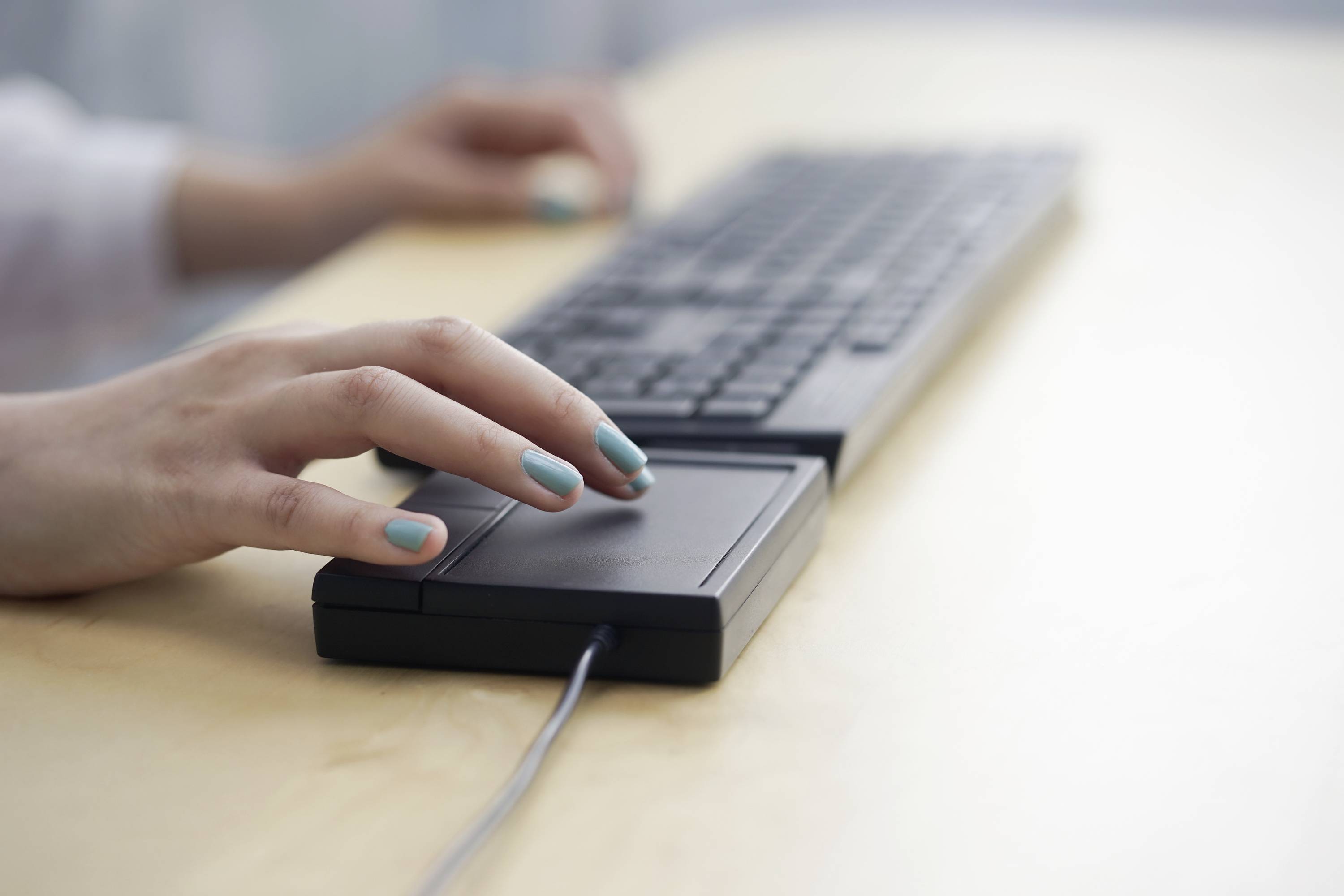 Een persoon typt op een computerkeyboard op een houten tafel. De focus ligt op de hand die de muis aanraakt.