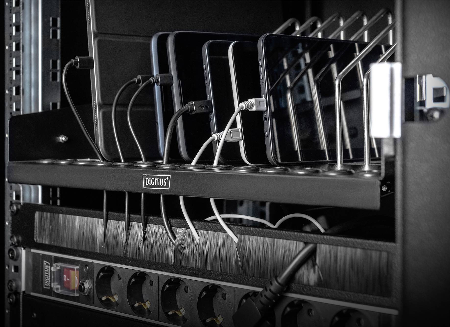 Mobiele telefoons worden opgeladen in een laadstation met meerdere USB-kabels. Het station bevindt zich in een IT-rack.