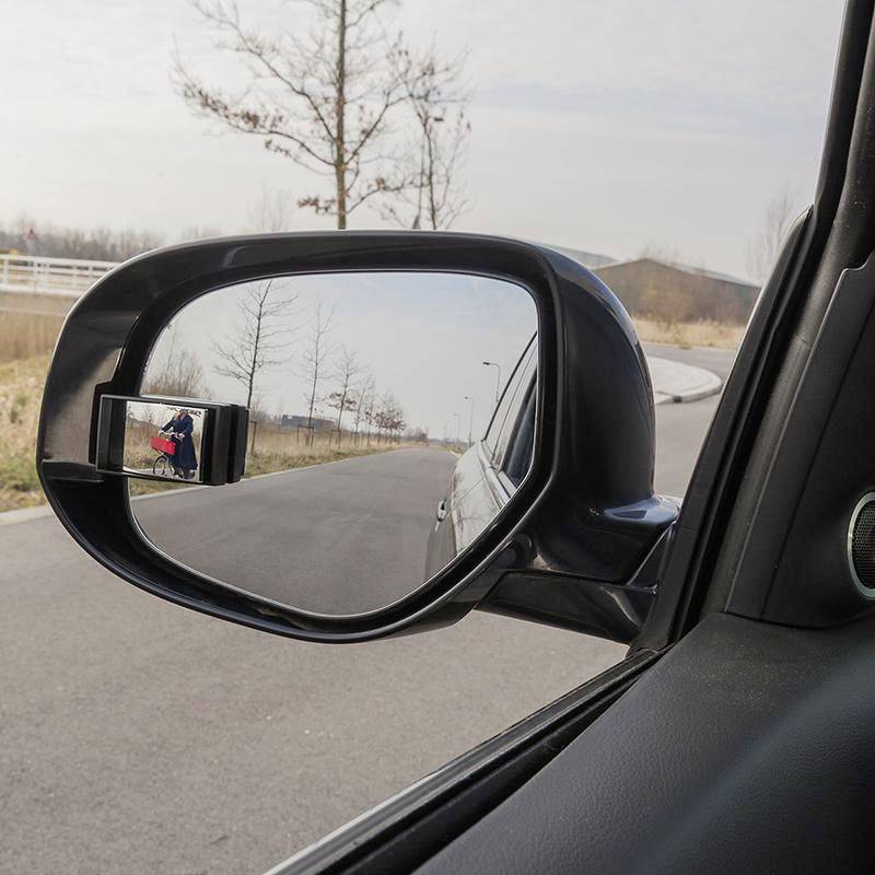 Een auto-buitenspiegel toont het uitzicht naar achteren op een lege landweg op een winterdag, met kale bomen langs de kant van de weg.