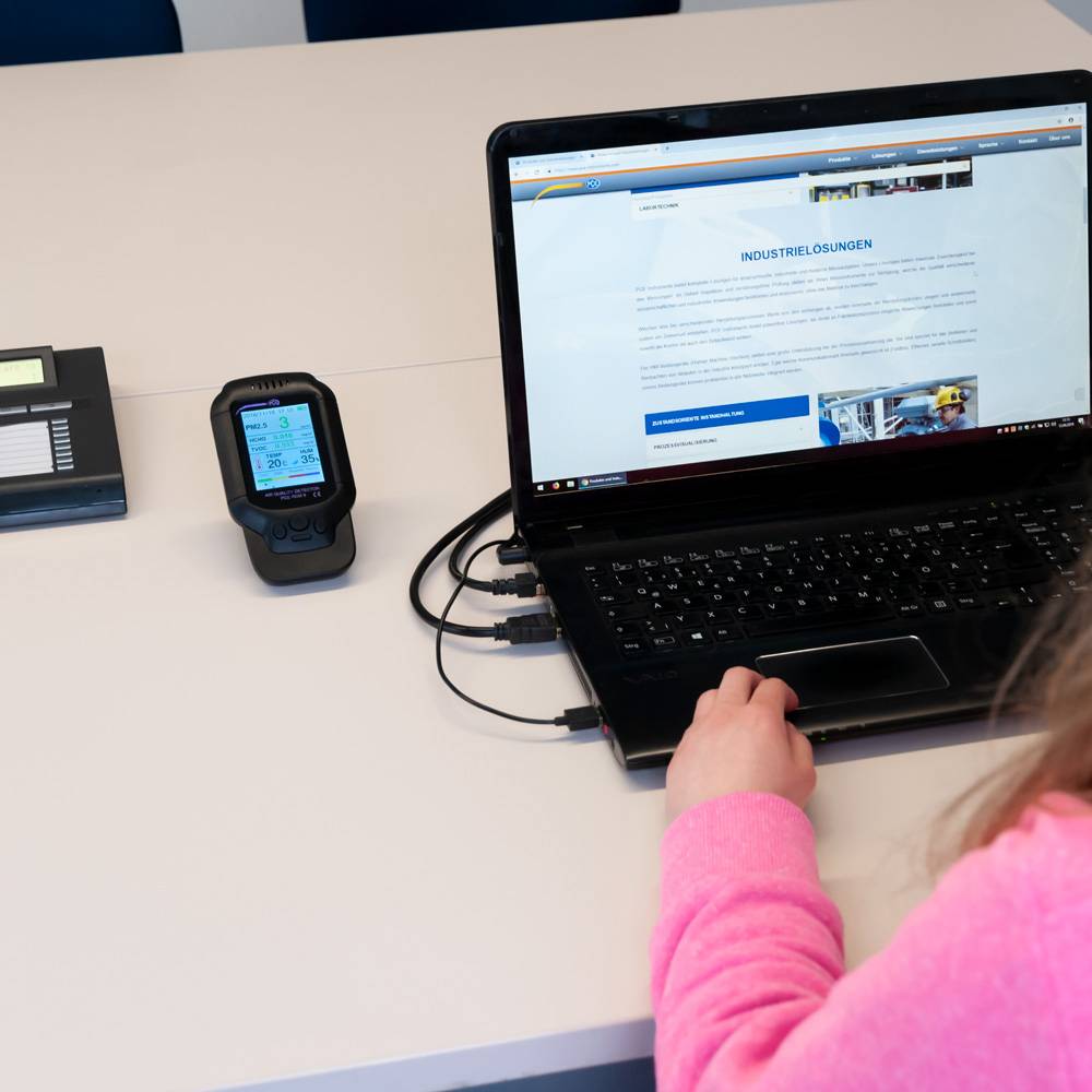 Een persoon typt op een laptop, naast een mobiel apparaat op een tafel. De laptop toont een website over industriële toepassingen.