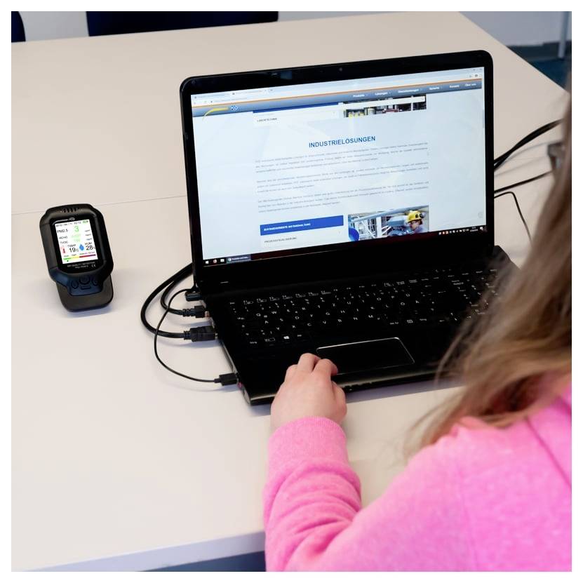Persoon die een laptop gebruikt die met een handheld apparaat op een bureau is verbonden, terwijl de laptop een Duitse 'Industrielösungen'-webpagina weergeeft.