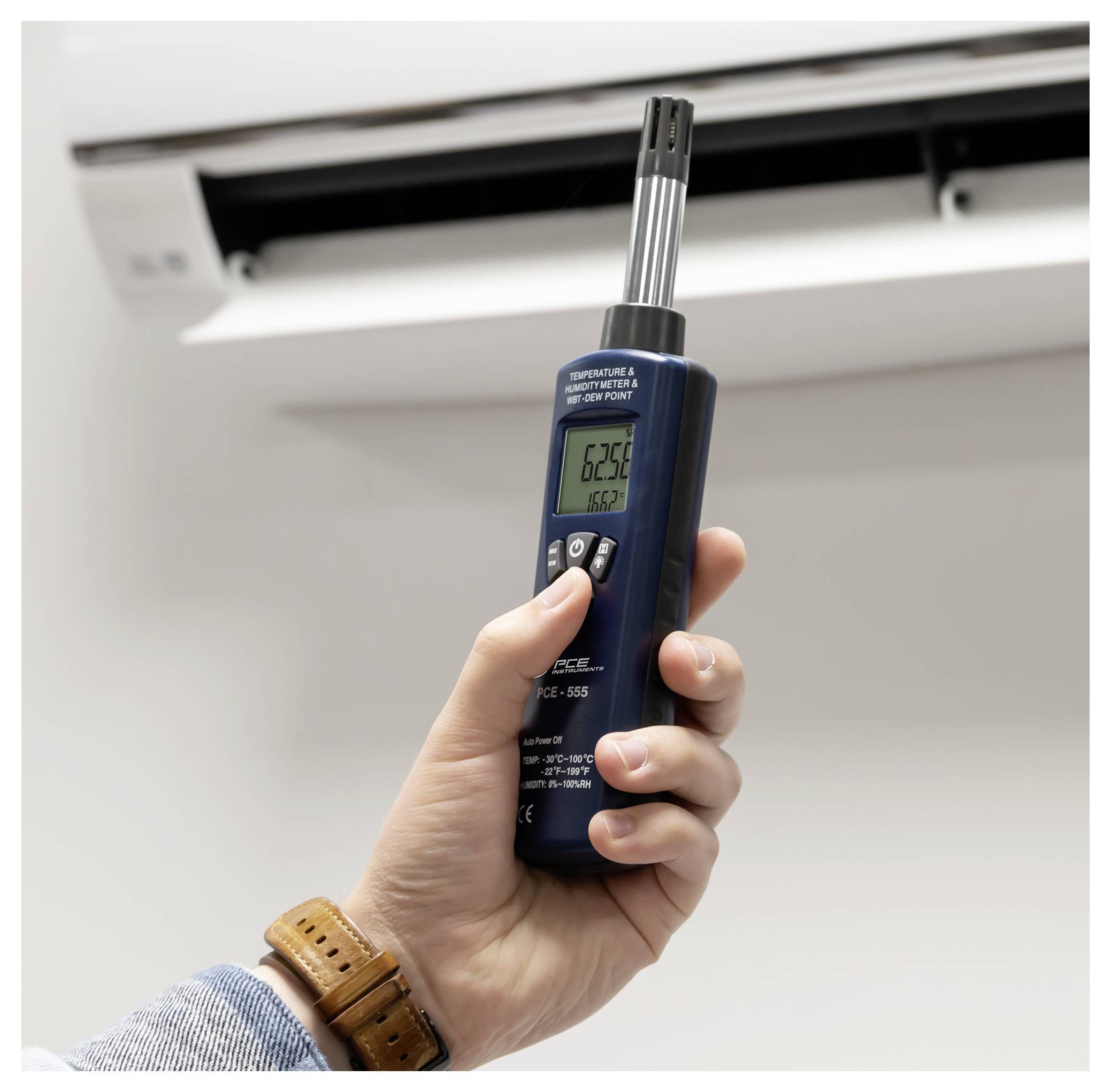 Hand die een digitale thermometer bij een airconditioner-ventilatieopening houdt, om de binnentemperatuur te meten.
