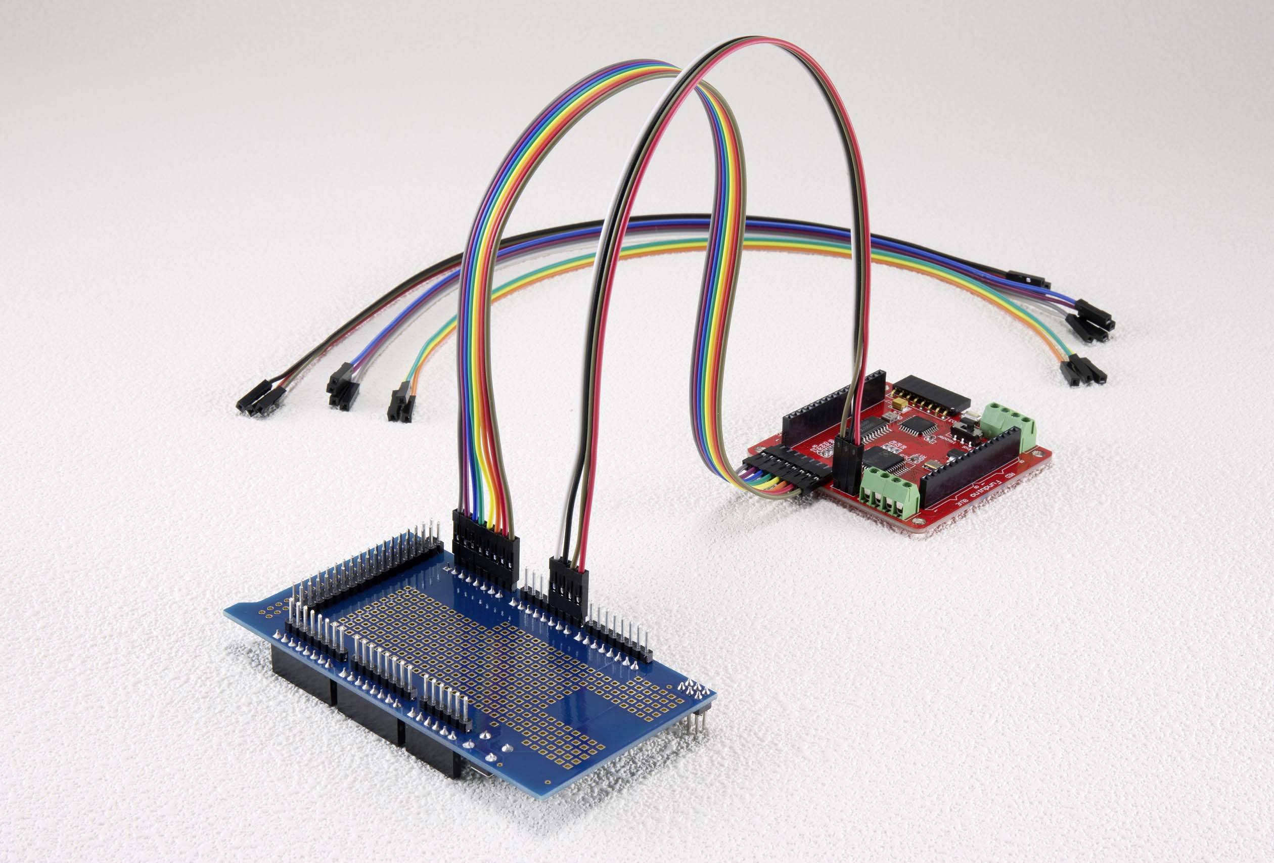 Twee elektronische printplaten zijn met gekleurde kabels verbonden. De voorste blauwe printplaat heeft vele pinnen, de achterste is rood.