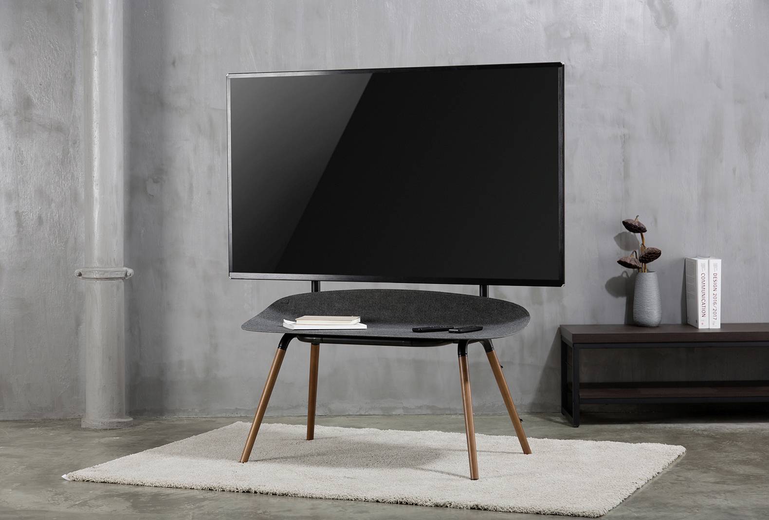 Een flatscreen-tv staat op een eenvoudige tafel met houten poten in een moderne, grijze ruimte.