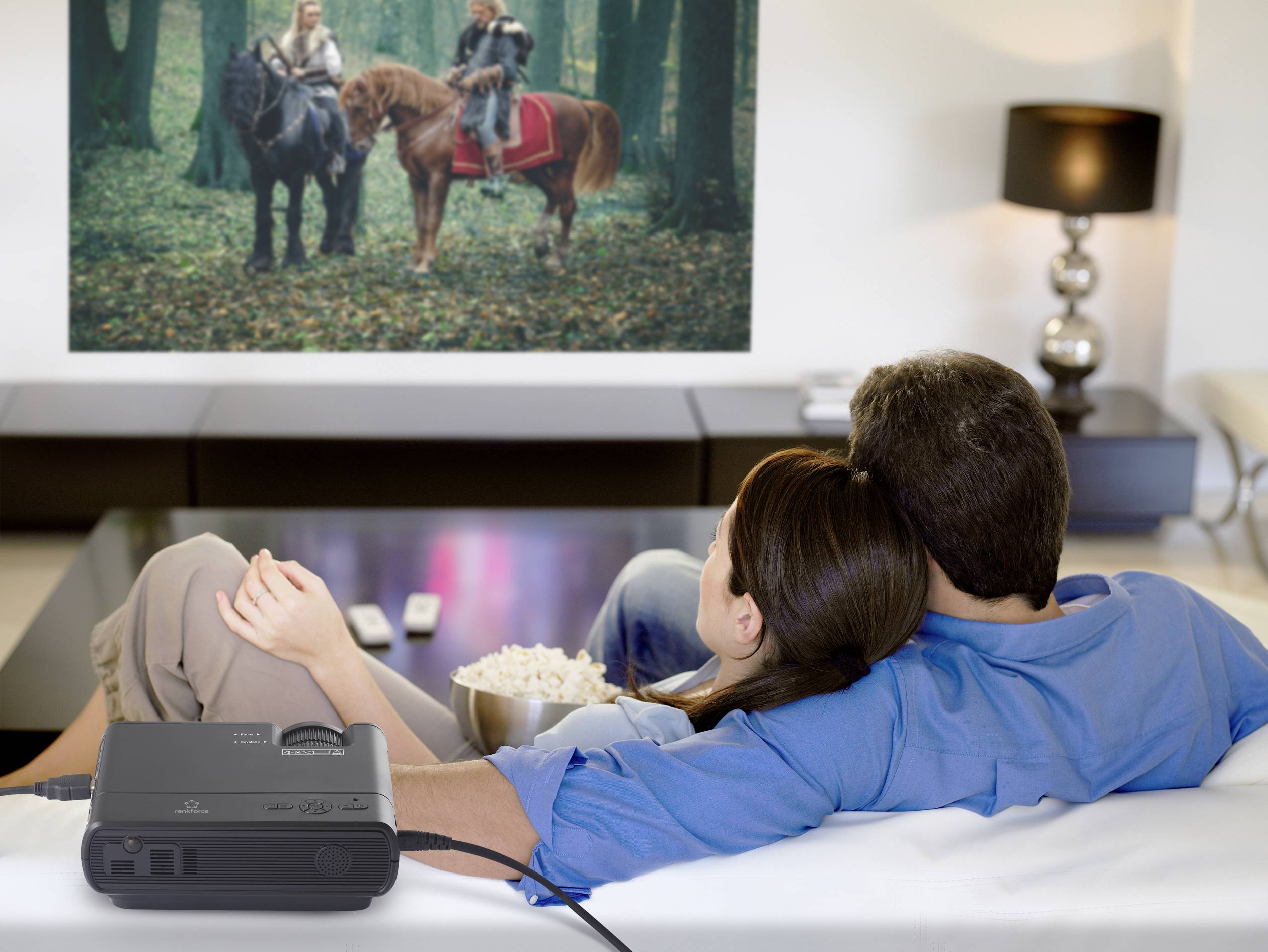 Een stel zit op een bank en kijkt naar een film met paardenmotieven op een scherm dat aan de muur wordt geprojecteerd.