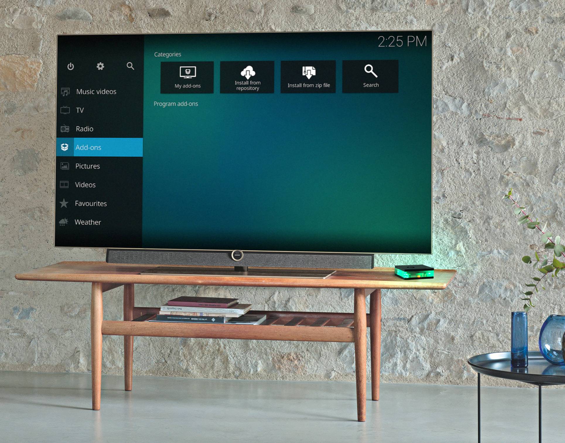 'Smart-tv op houten tafel, toont menuscherm met categorieën zoals muziekvideo's, afbeeldingen en add-ons. Tijd: 14:25.'