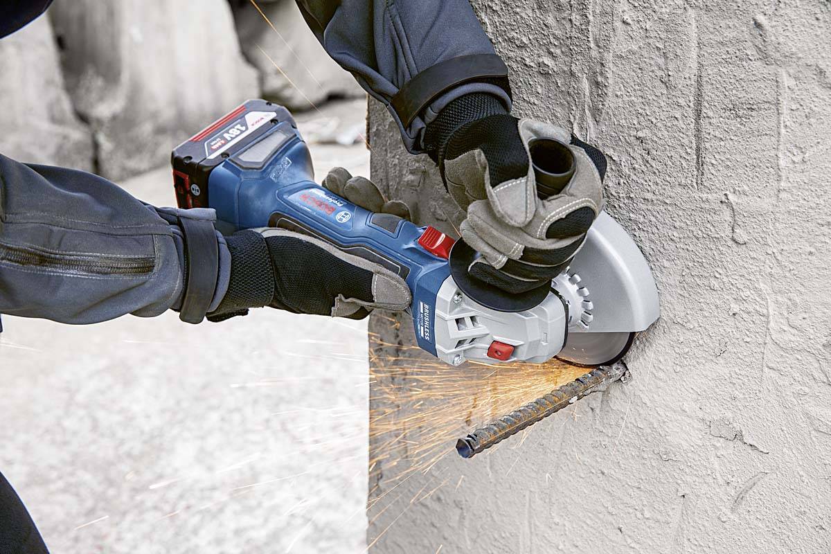 Een persoon snijdt beton met een blauwe haakse slijper. Vonken vliegen rond terwijl metalen staven worden doorgesneden.