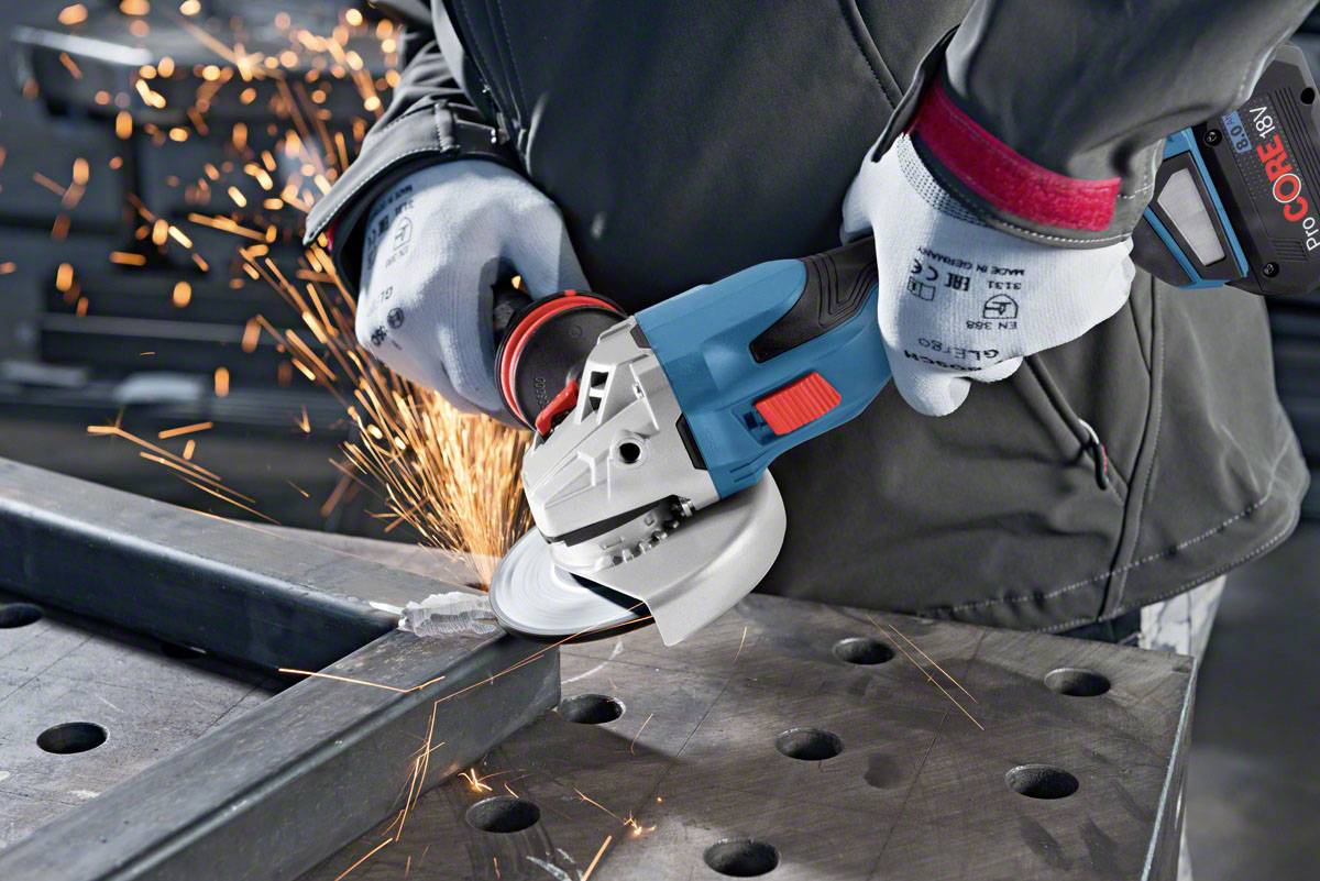 Een persoon bewerkt een metalen voorwerp met een haakse slijper, waarbij vonken neerdalen. Ze draagt veiligheidskleding en handschoenen.