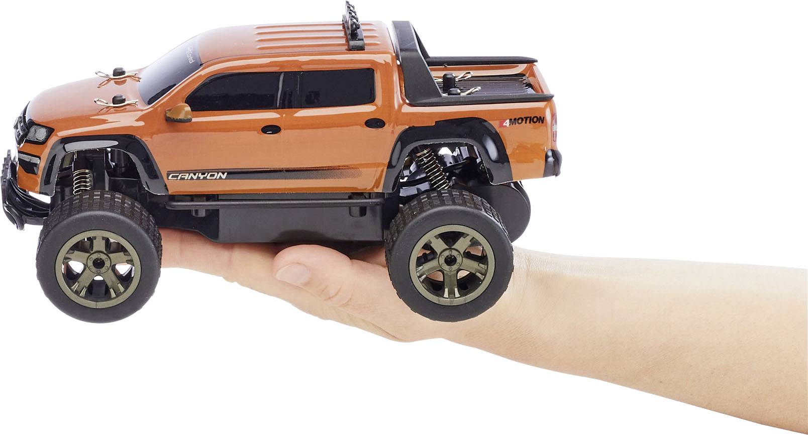 Een oranje modelauto in SUV-stijl wordt op een hand gepresenteerd. Het heeft grote wielen en een sportieve uitstraling.