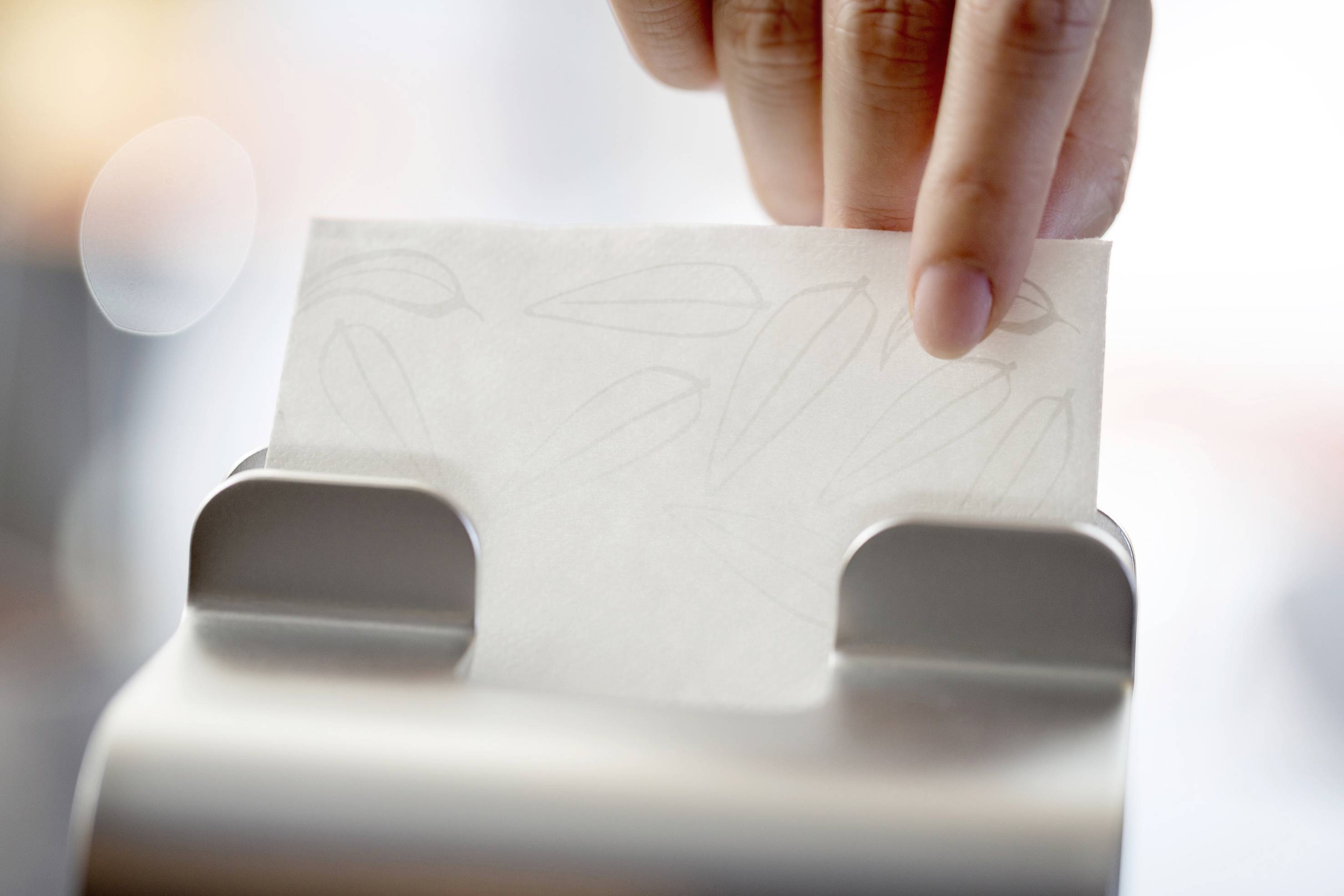 Een hand trekt een enkel papieren doekje uit een dispenser.