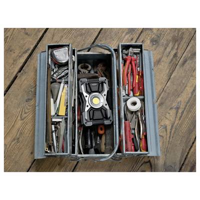 Open blauwe gereedschapskist georganiseerd met handgereedschap, inclusief een draagbaar werklicht in het midden, tang, schroevendraaiers, tape en ander gereedschap op een houten vloer.