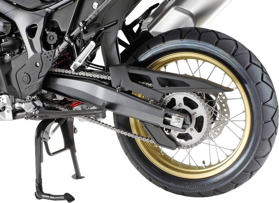 Achterwiel van een motorfiets met gouden velg en grove profielband. De ketting en het remsysteem zijn zichtbaar.