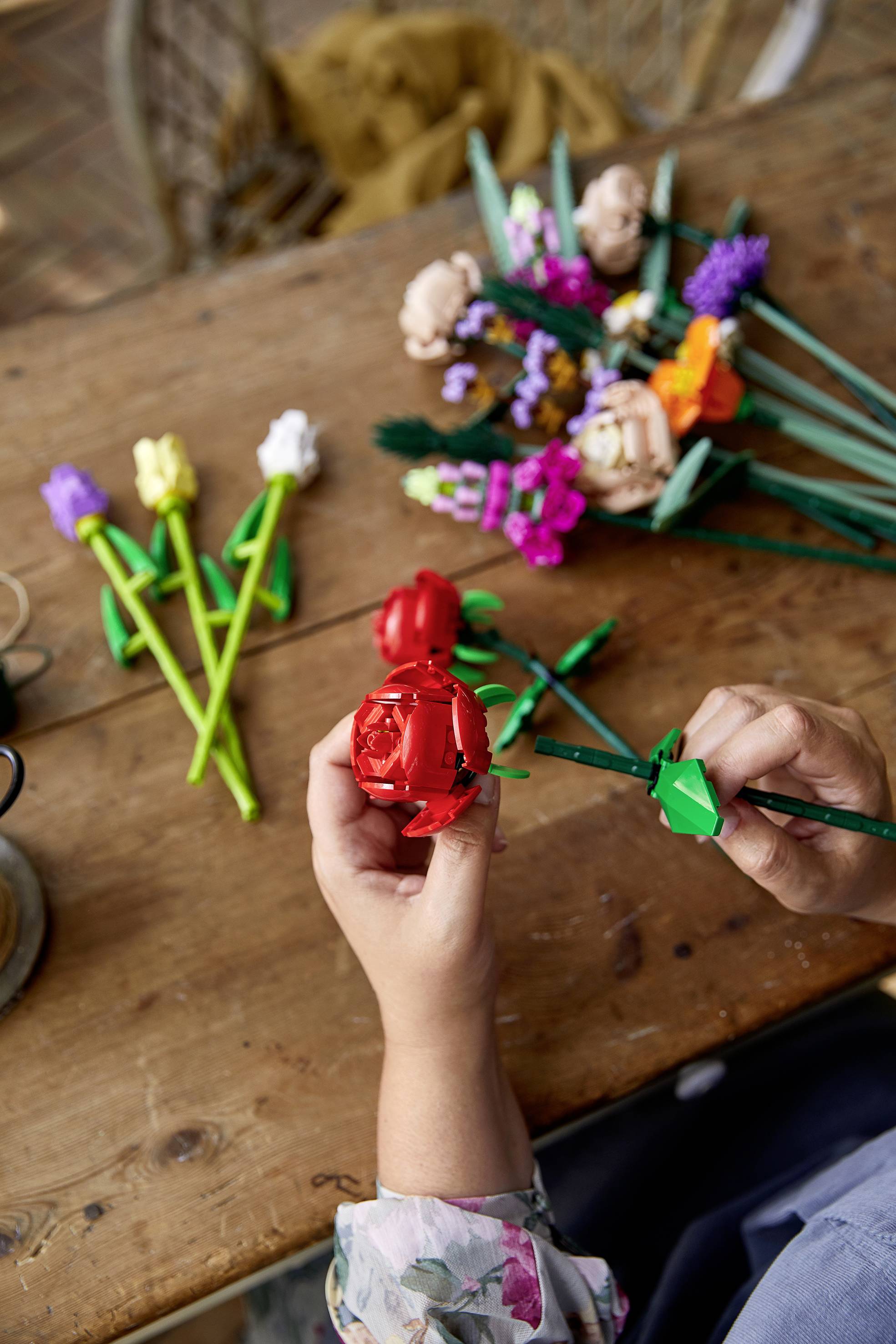Een persoon maakt bloemen van gekleurd papier op een houten tafel, met afgewerkte boeketten op de achtergrond.