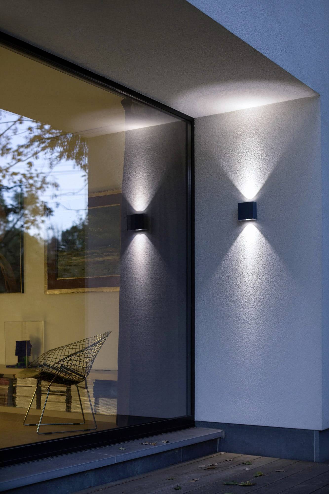 Modern gebouw met grote raampartijen en stijlvolle buitenverlichting die geometrische patronen op de muur projecteert.