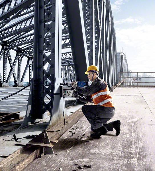 Een bouwarbeider met een veiligheidshelm werkt aan een ijzeren brug en gebruikt een meetapparaat. De brug strekt zich uit tot aan de horizon.
