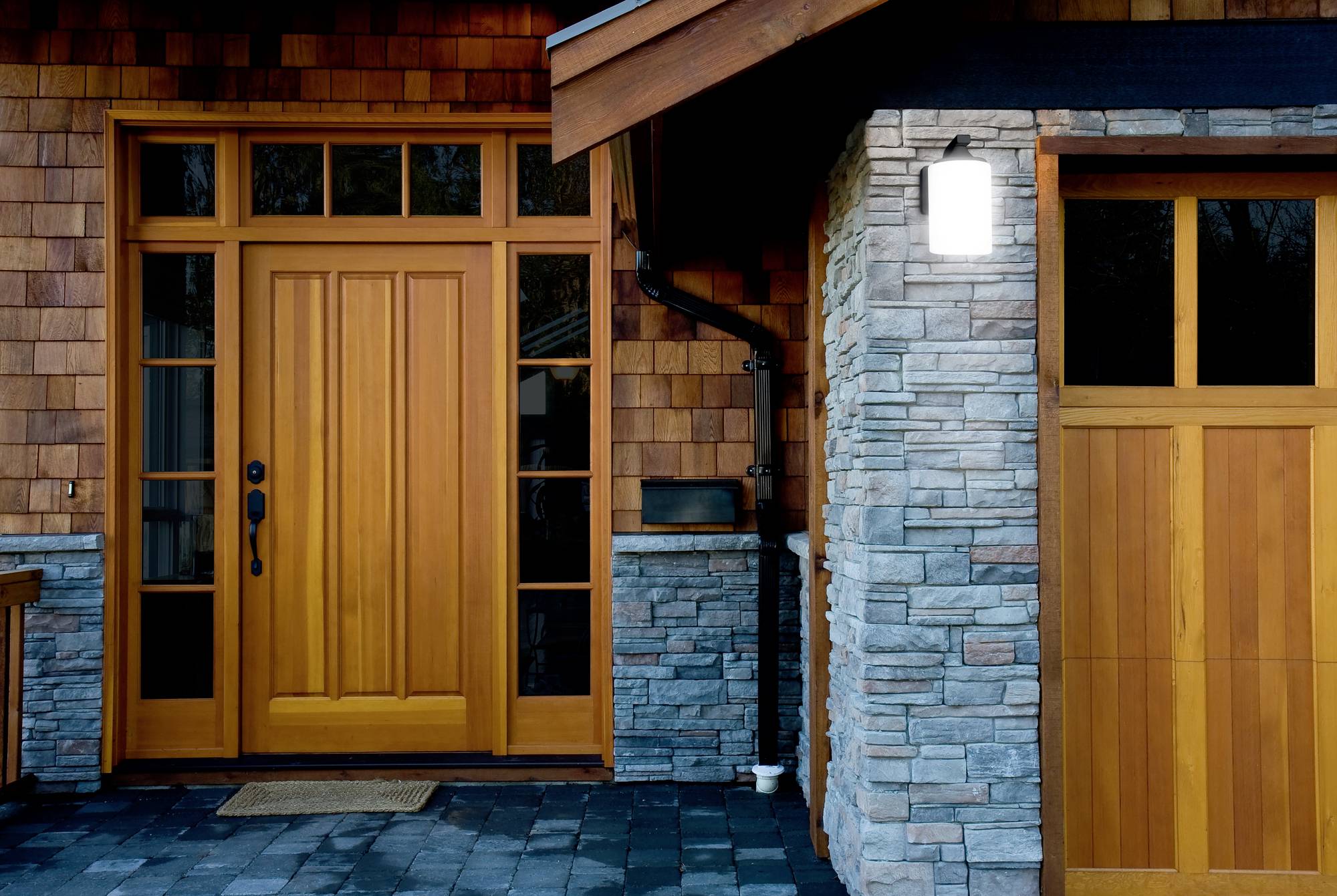 Ingang van een houten hut met een houten voordeur, geflankeerd door grote ramen en steenbekleding op de muur.