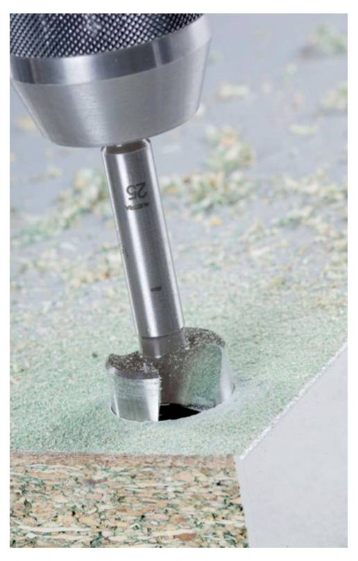 Een metaalboor boort een rond gat in een houten plank. Houtkrullen liggen rond het gat verspreid.