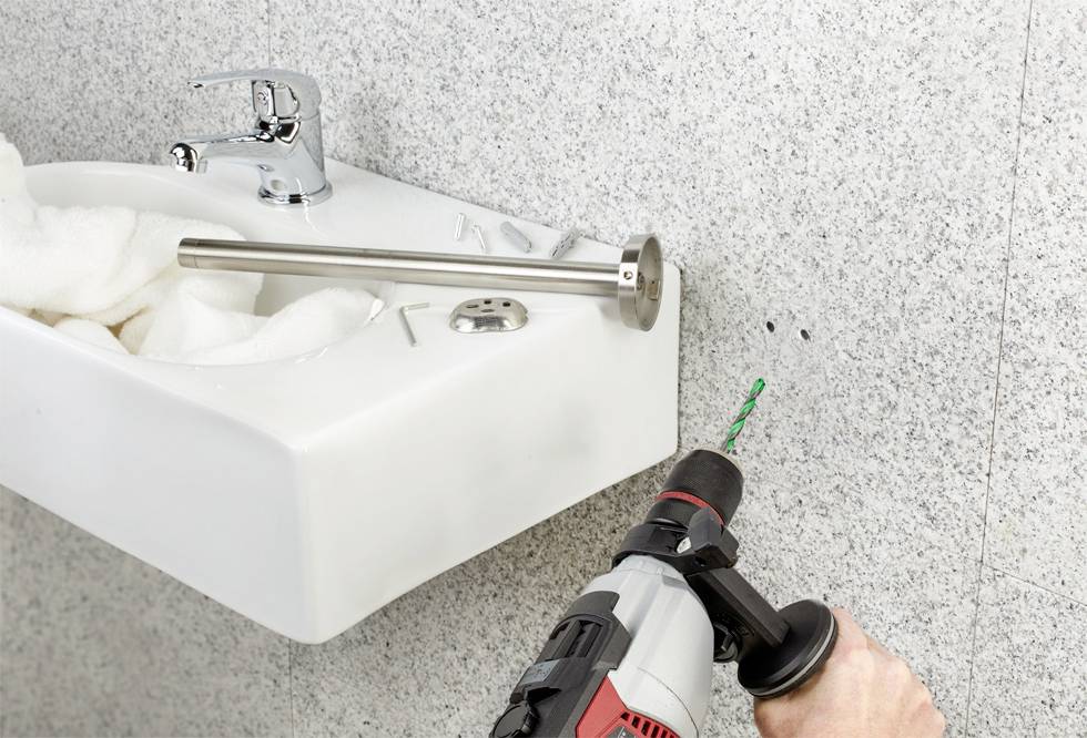 Een wasbak wordt gemonteerd aan een granieten muur. Iemand boort gaten in de muur naast de wasbak voor de bevestiging.